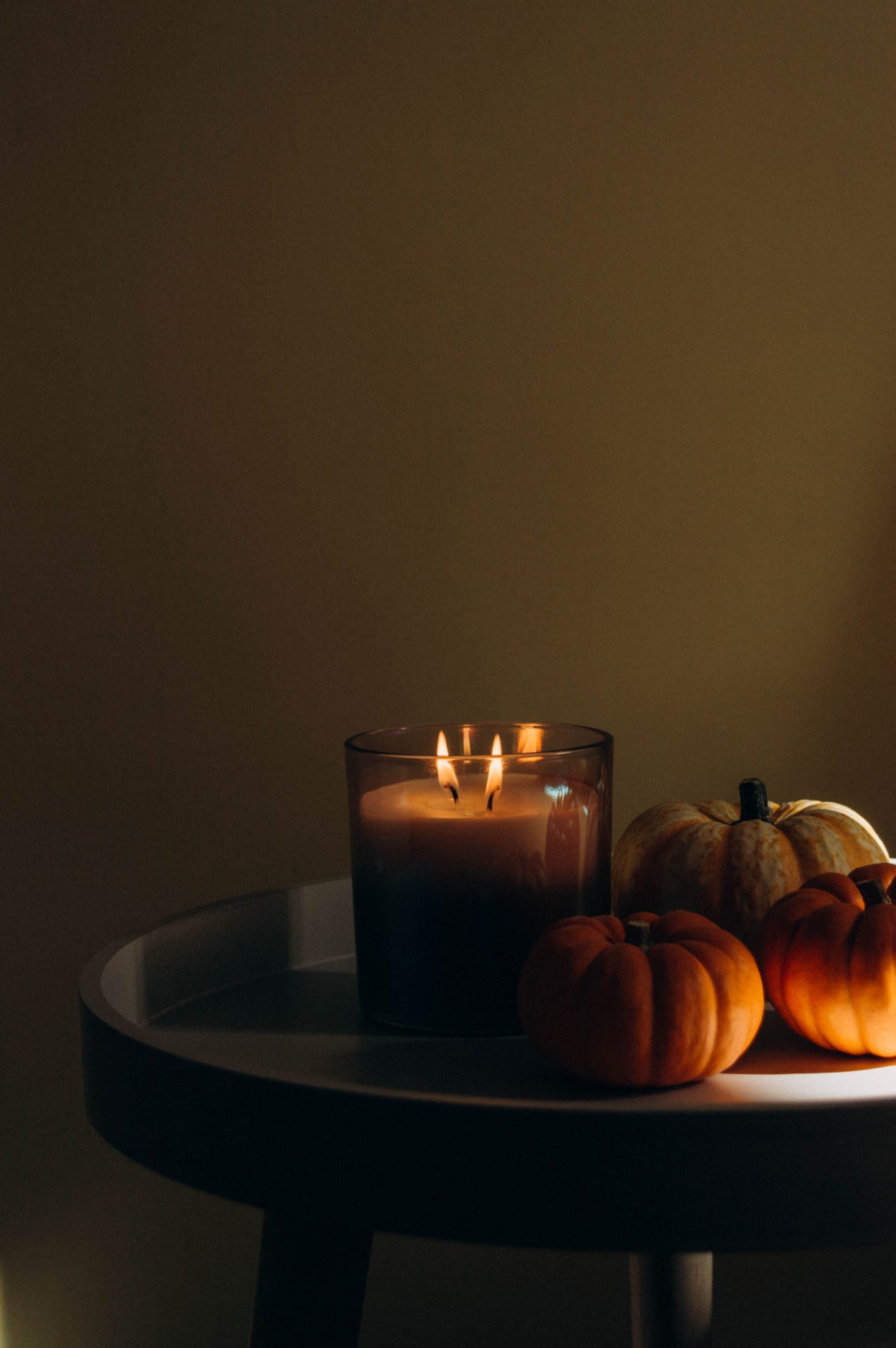 Warm candlelight with small pumpkins on a table creates a cozy autumn atmosphere.