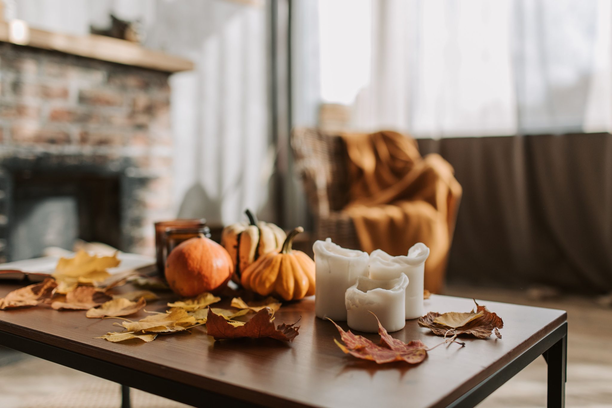 Warm indoor autumn setting with candles, pumpkins, and dried leaves on a wooden table, creating a cozy atmosphere.