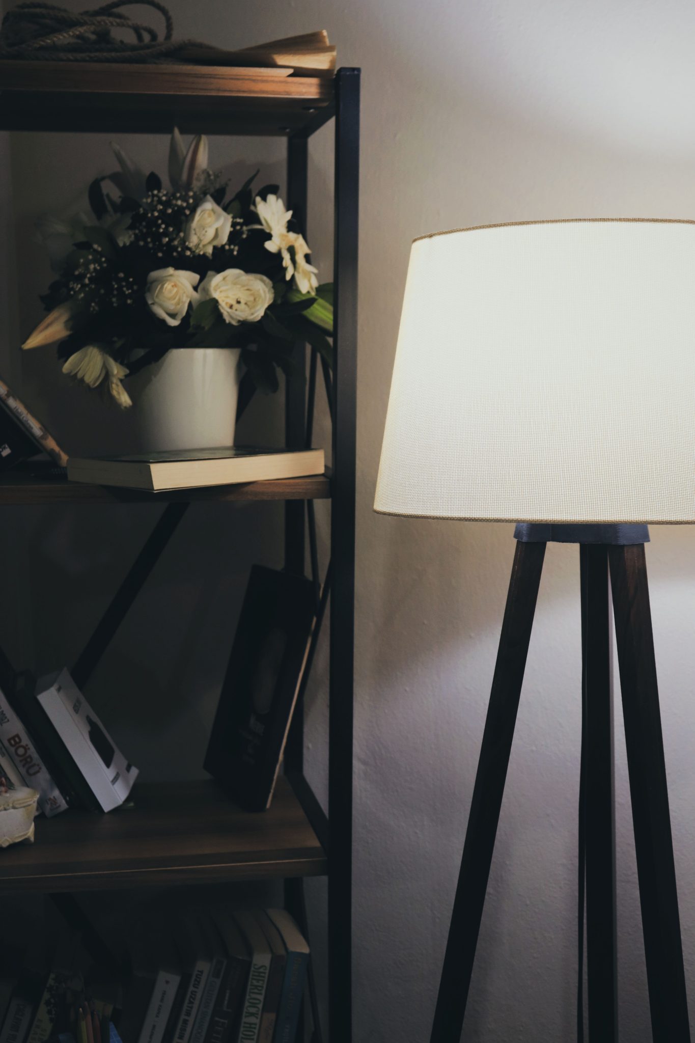 Warmly lit lamp beside a bookshelf with flowers and books, perfect for a cozy reading corner.