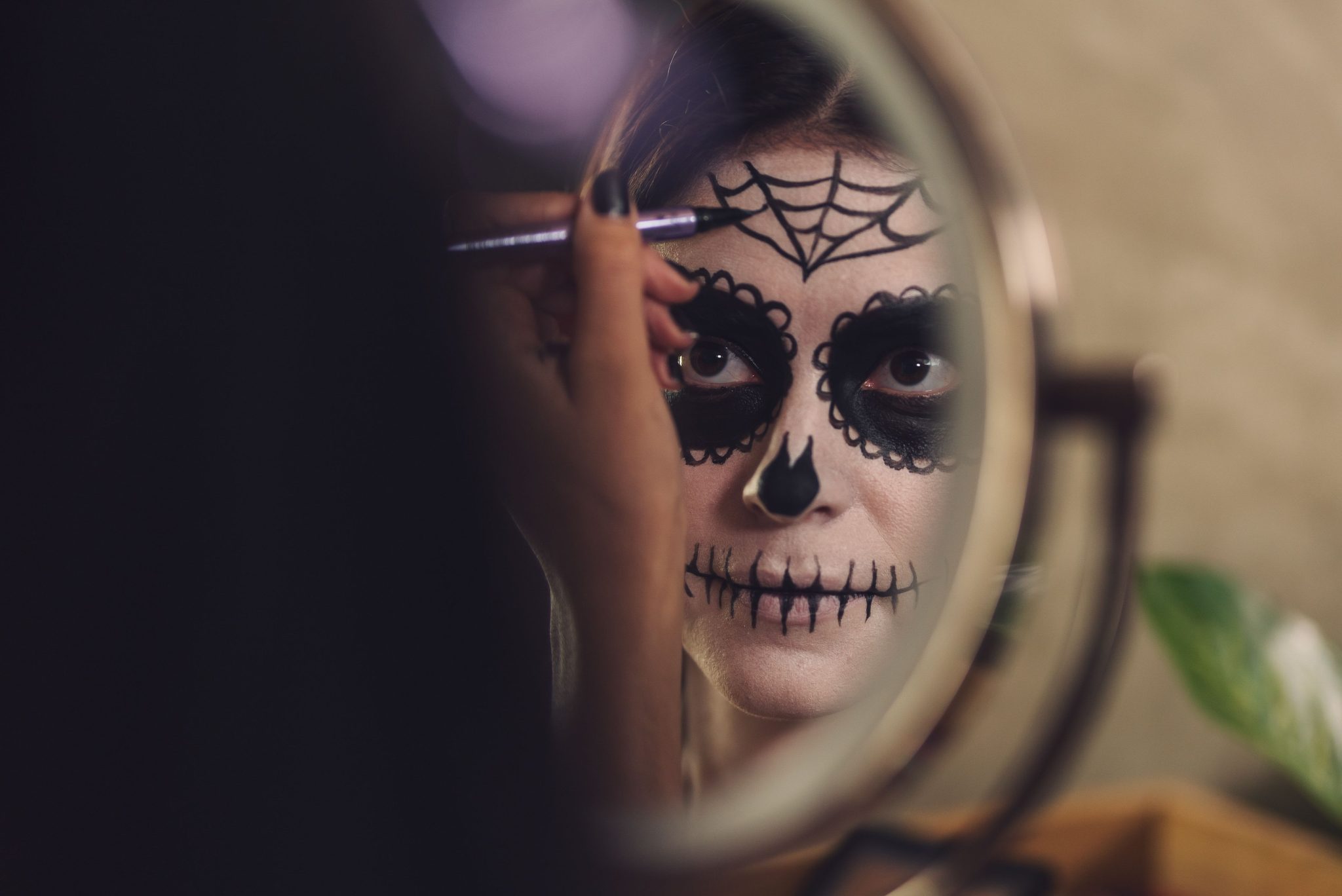 Woman in front of mirror applying Day of the Dead face paint for Halloween celebration.