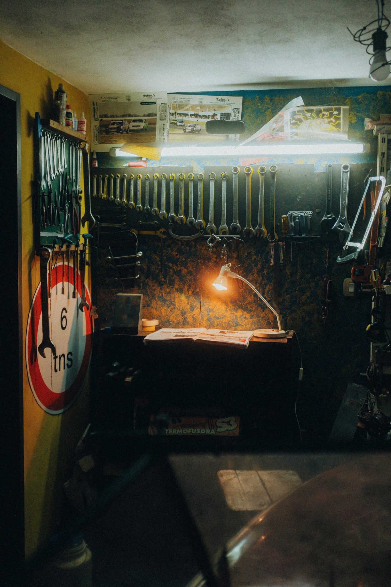Workshop full of tools placed in perfect order of size. Tube lighting and a lamp create color separation. The walls are decorated with signs and posters.