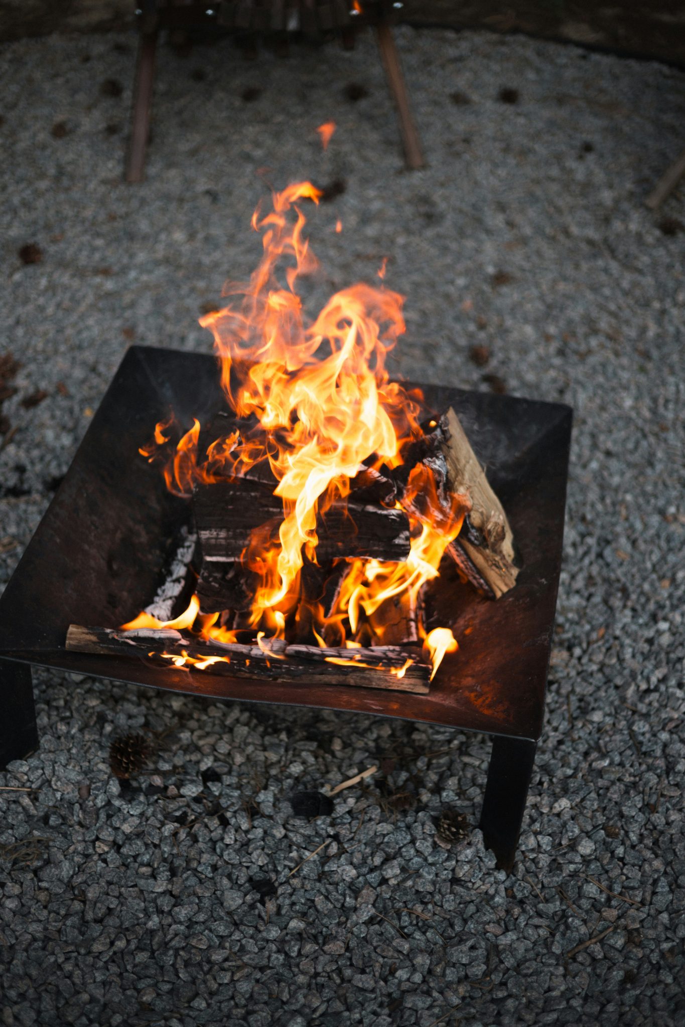 A bright fire burning in a metal fire pit on grey gravel