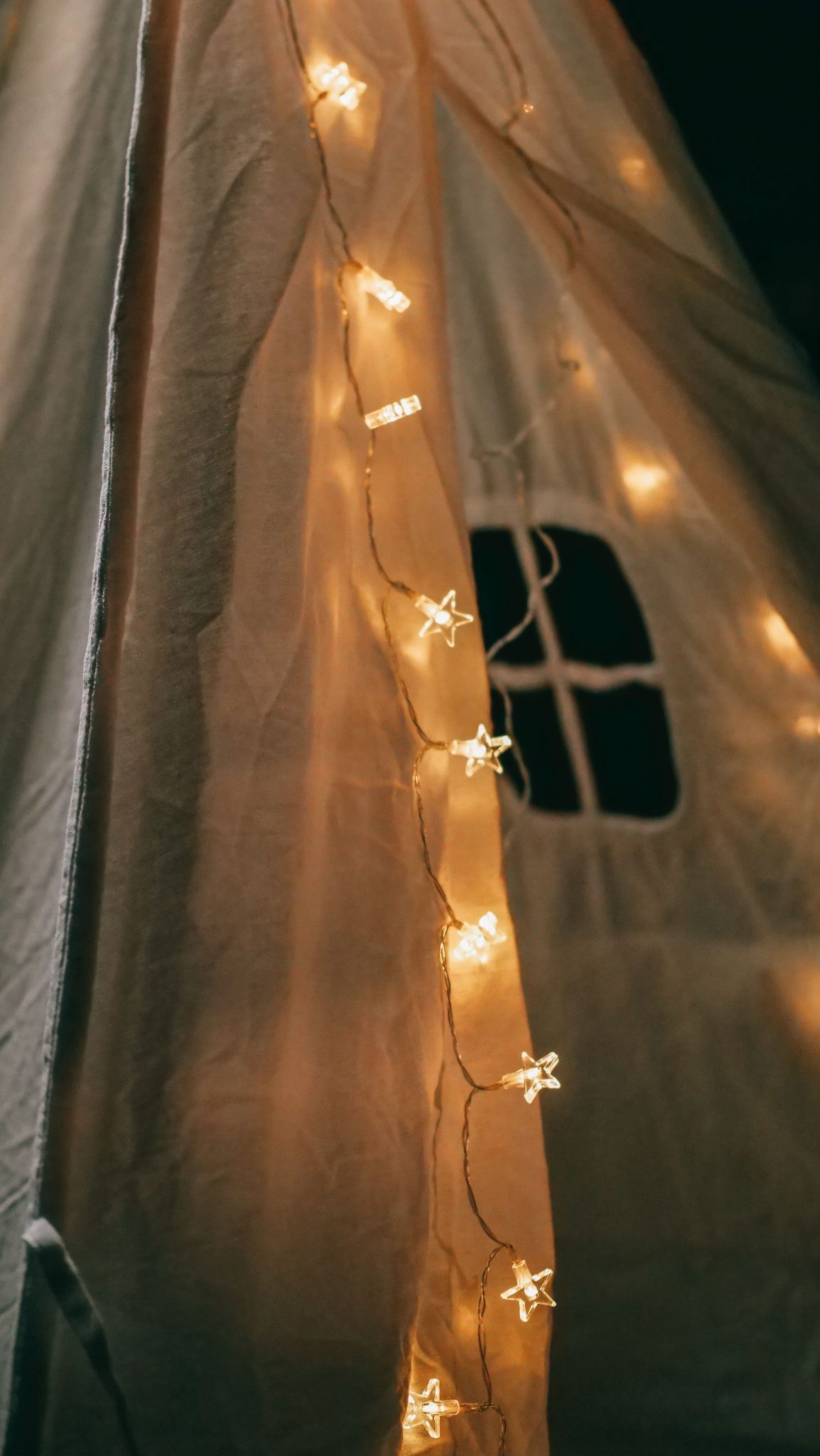 A cozy close-up of a teepee adorned with star-shaped string lights glowing softly at night.