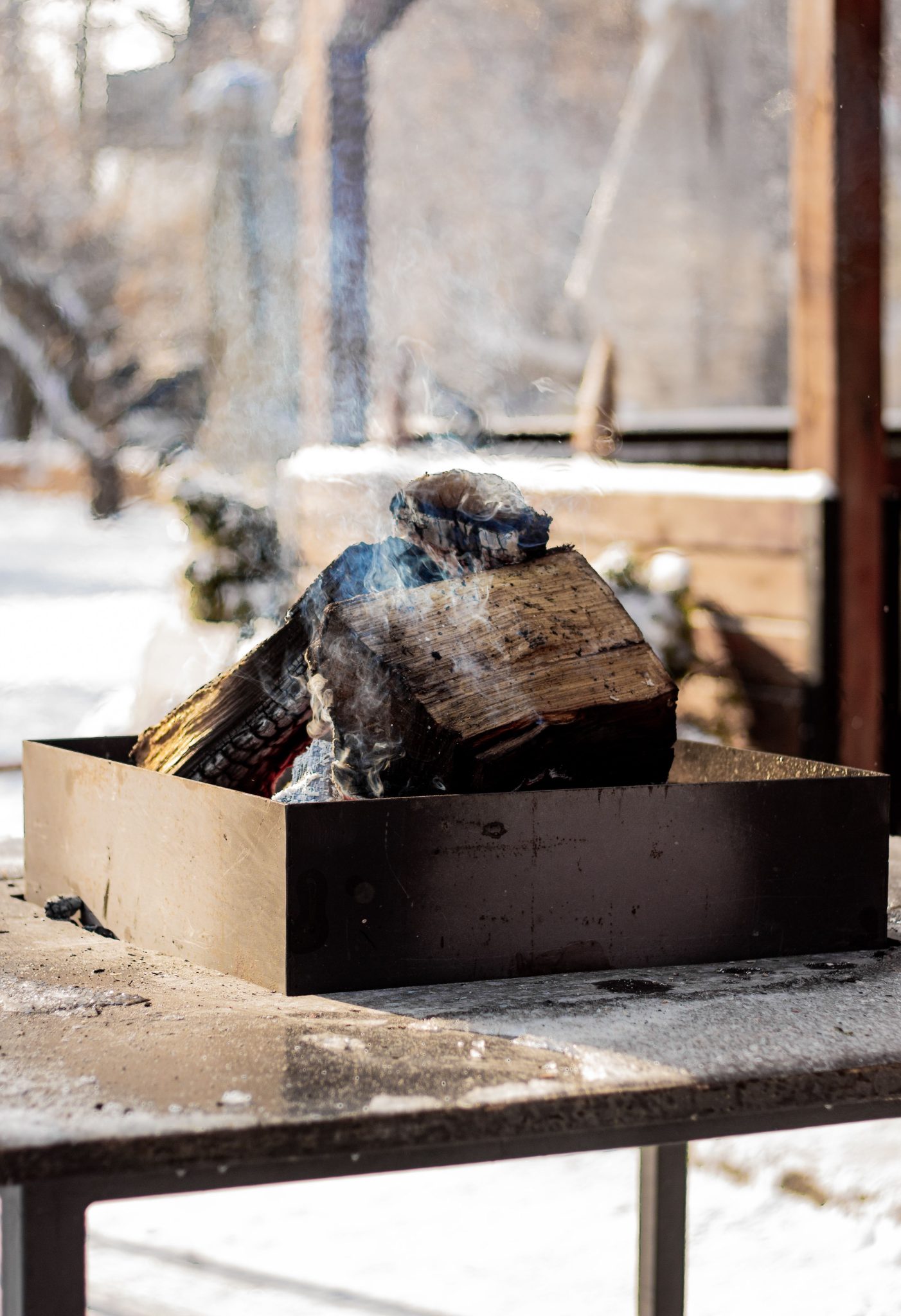 A cozy fire pit with smoking logs outdoors on a snowy winter day, exuding warmth and comfort.