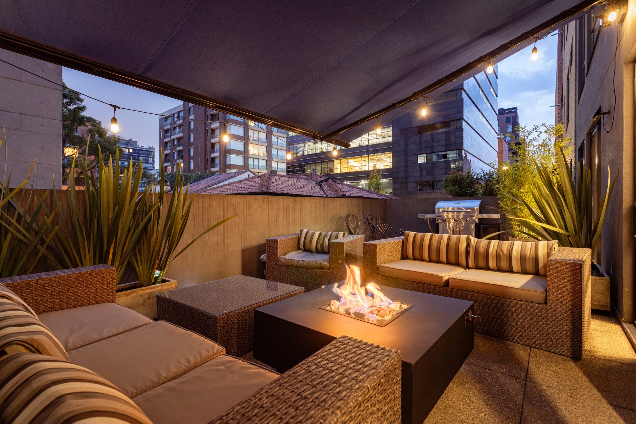 A cozy urban patio setting with elegant furniture and a glowing fire pit during twilight.
