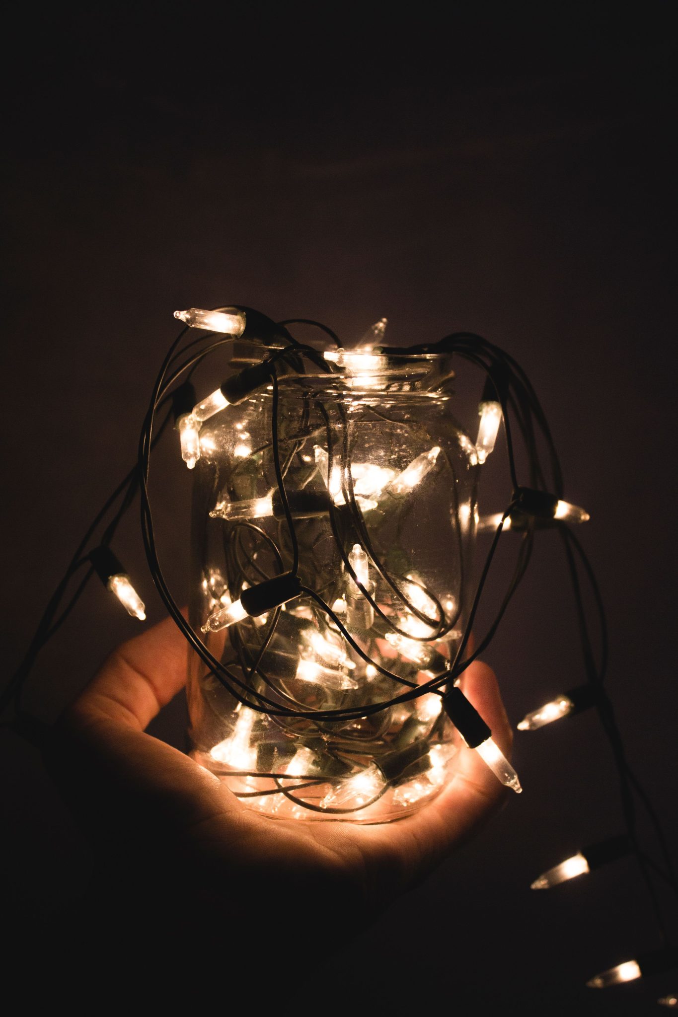 A glass jar full of glowing Christmas lights held in a hand, creating a warm ambiance.