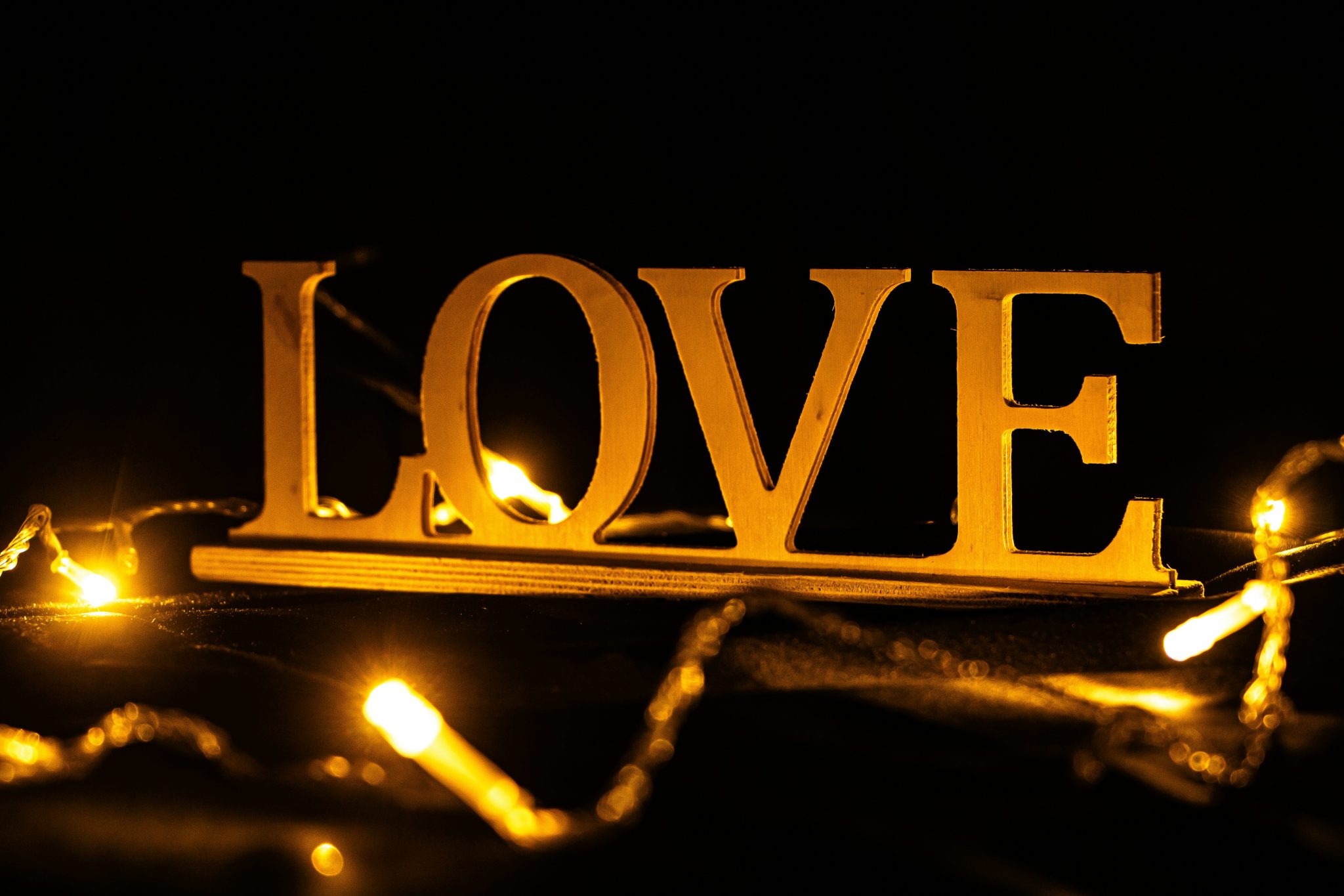 A glowing wooden 'LOVE' sign illuminated by warm yellow string lights stands out against a dark backdrop.