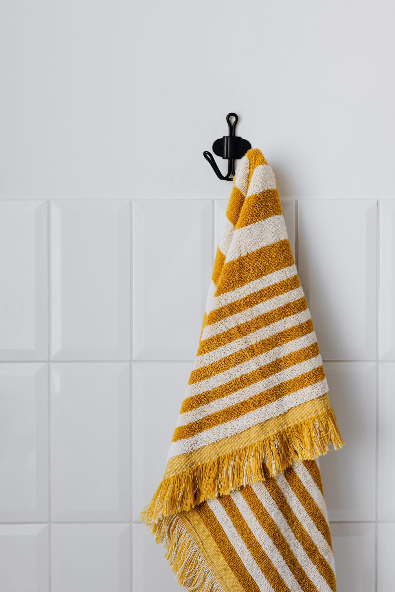 A stylish striped yellow and white towel hanging on a wall hook in a bathroom setting.