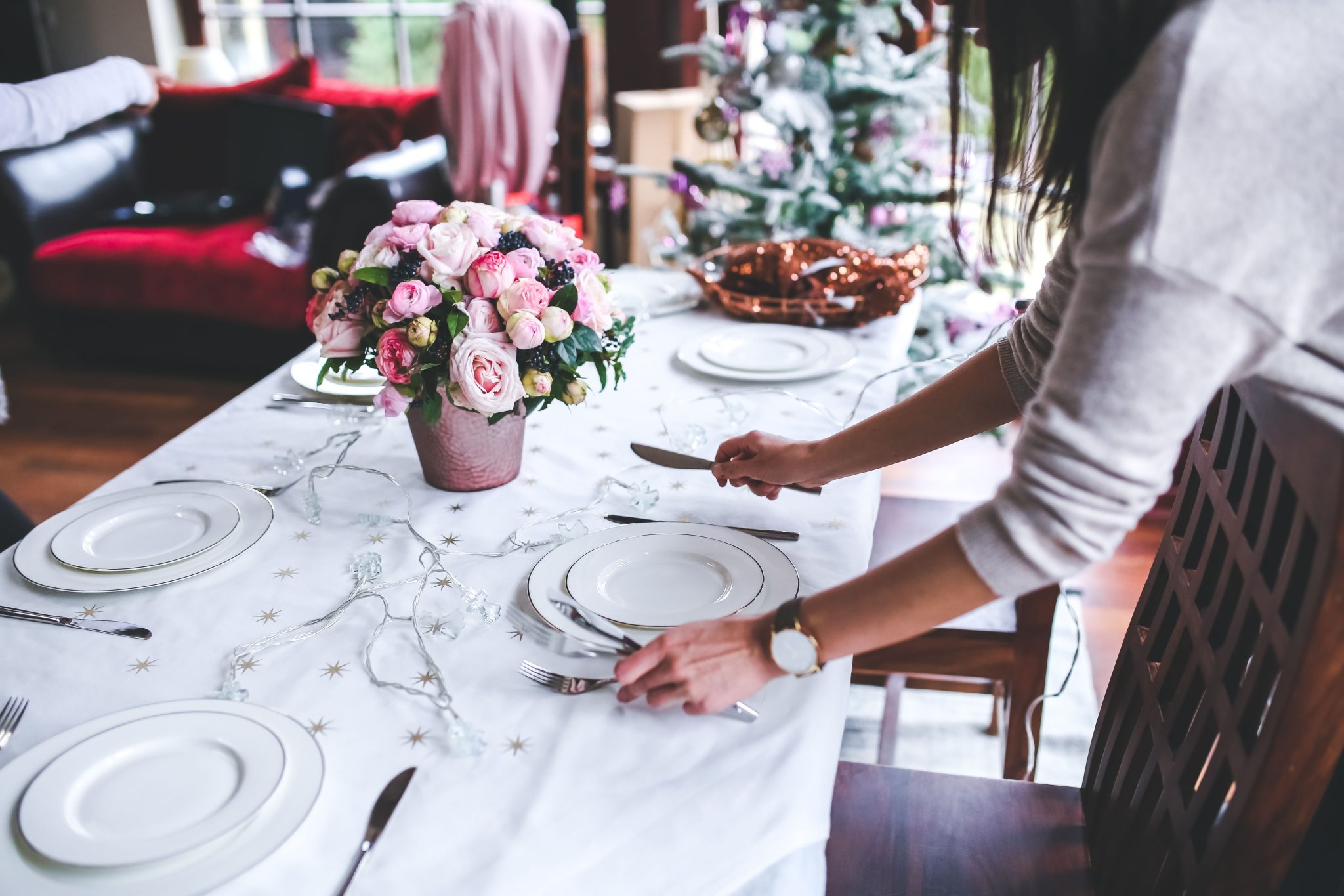 A woman sets a beautifully decorated dining table with flowers for a festive occasion indoors.