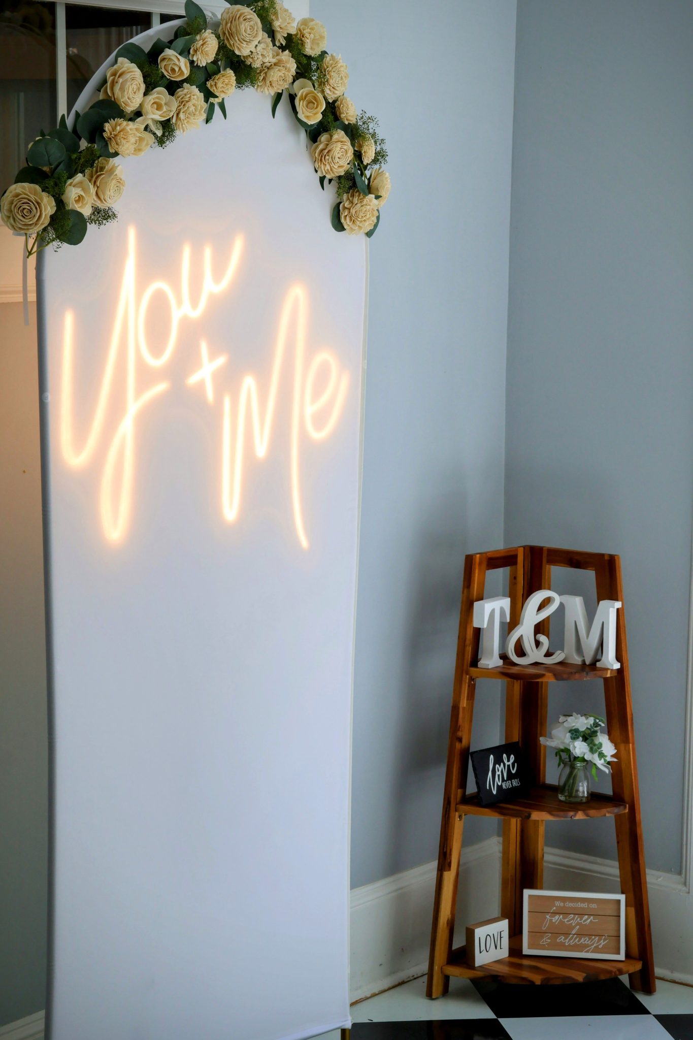 An illuminated 'You + Me' wedding sign adorned with flowers, perfect for romantic events.