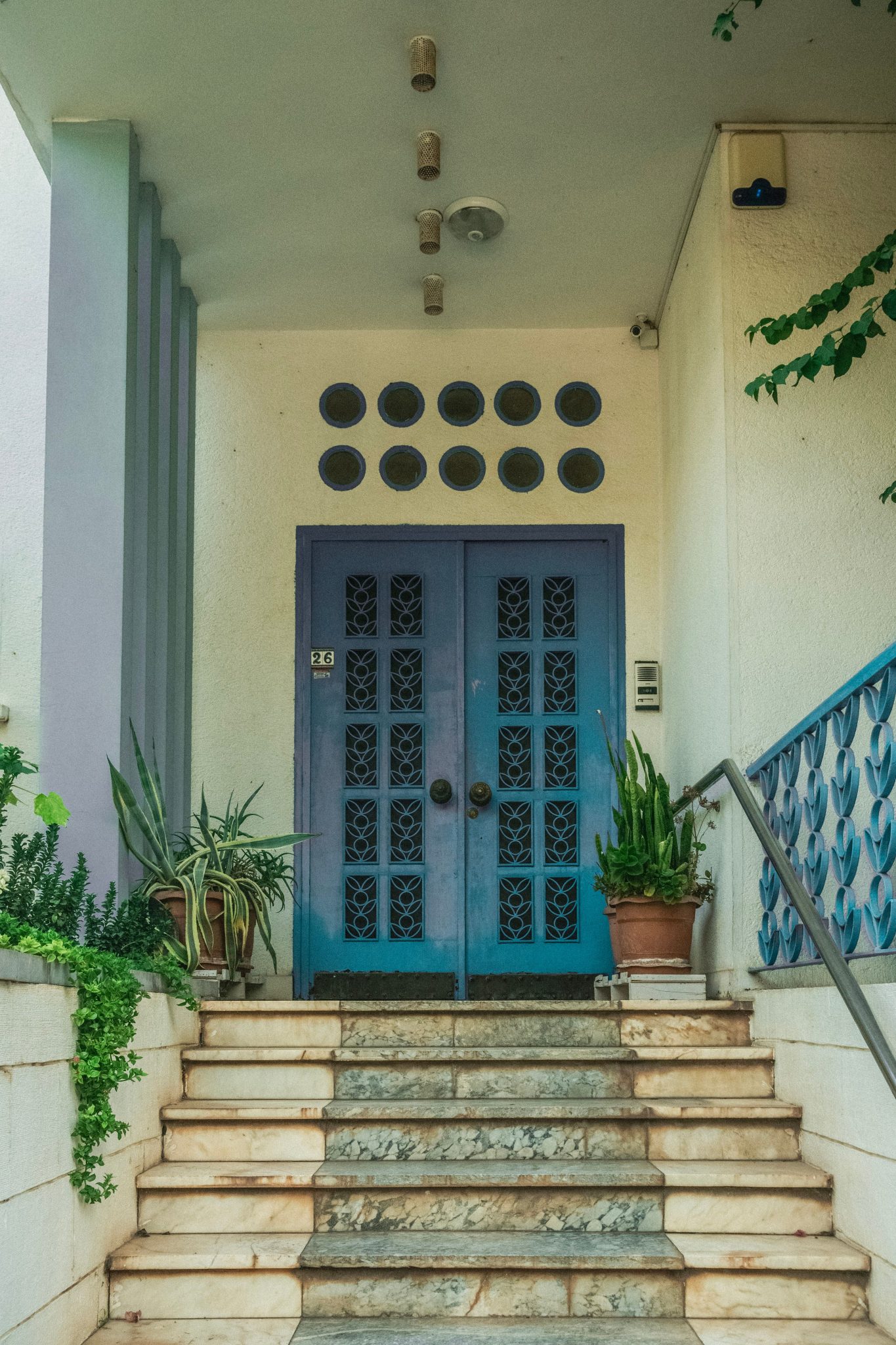 An inviting entrance featuring striking blue double doors framed by greenery and stone steps.