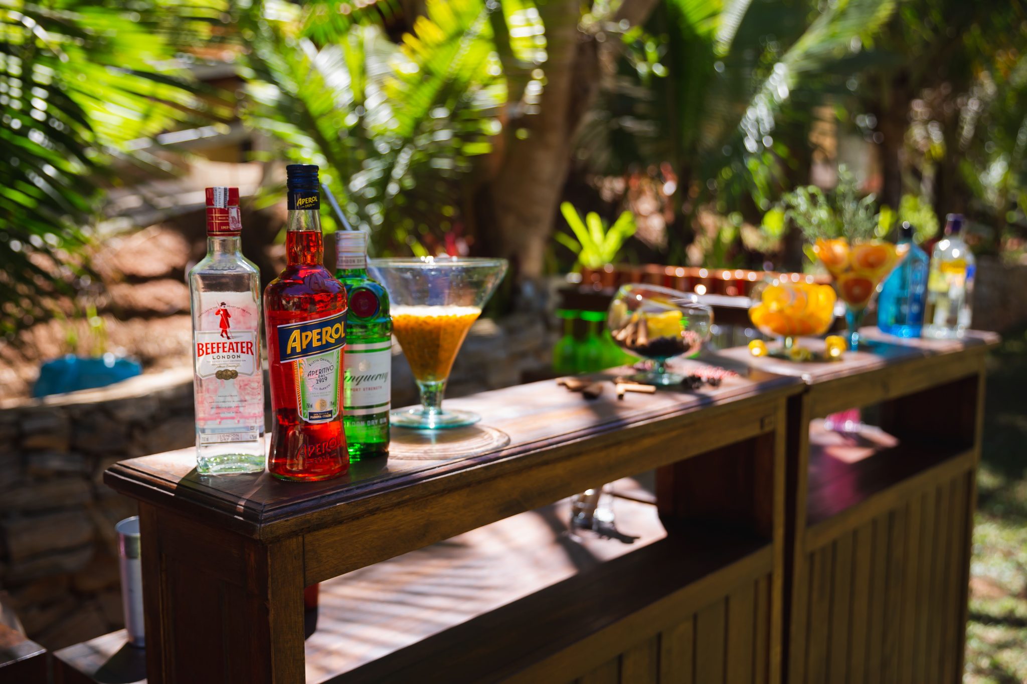 Bright outdoor bar scene with cocktails and spirits on wooden counter.