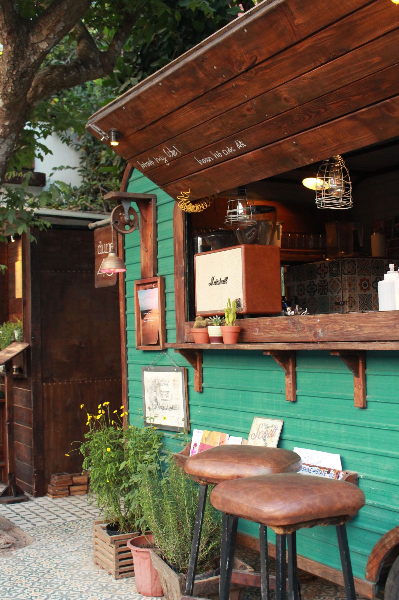 Charming outdoor coffee bar with rustic wooden decor, greenery, and stools for a cozy atmosphere.
