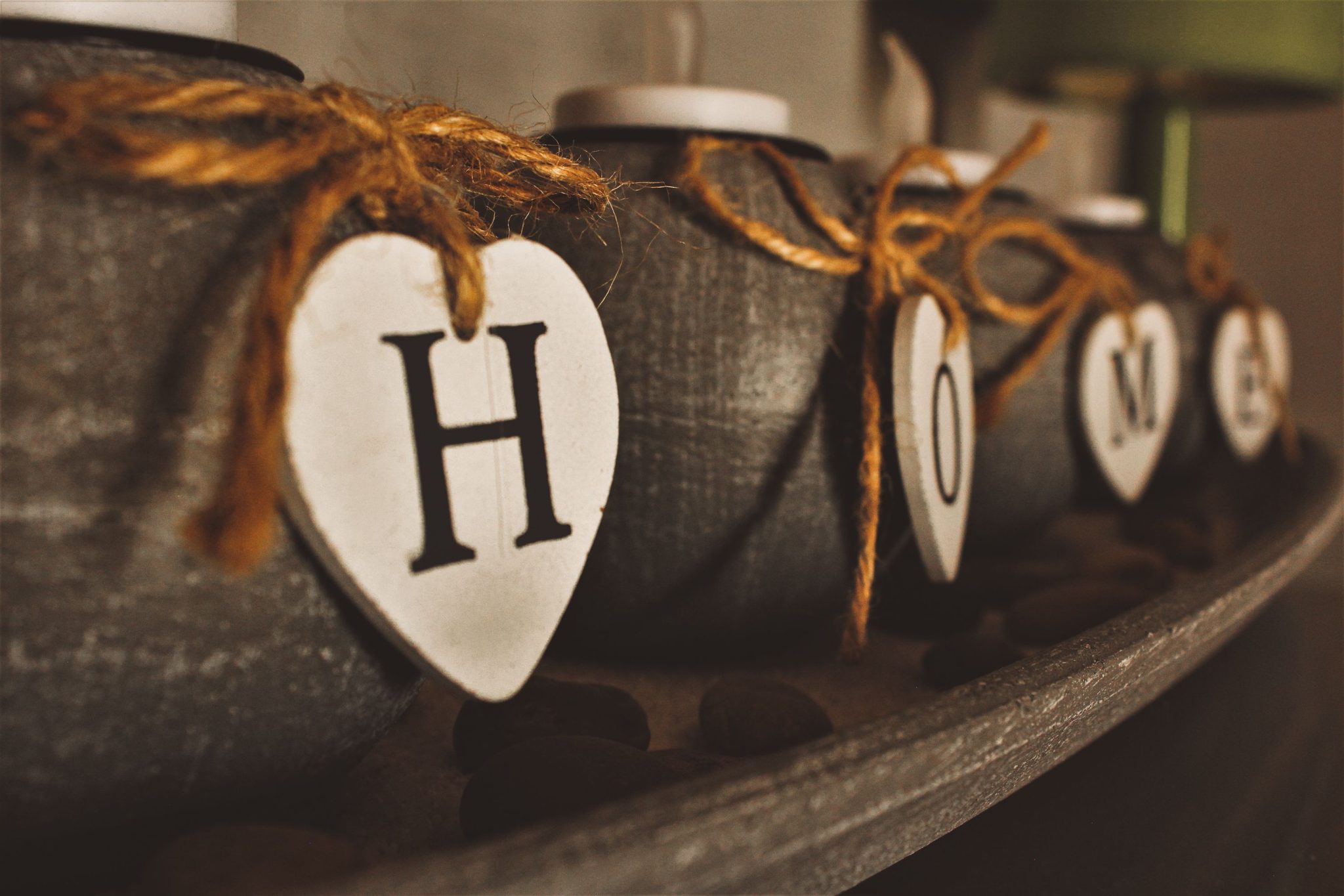 Close-up of rustic heart-shaped tags spelling 'HOME' on decorative jars tied with twine.