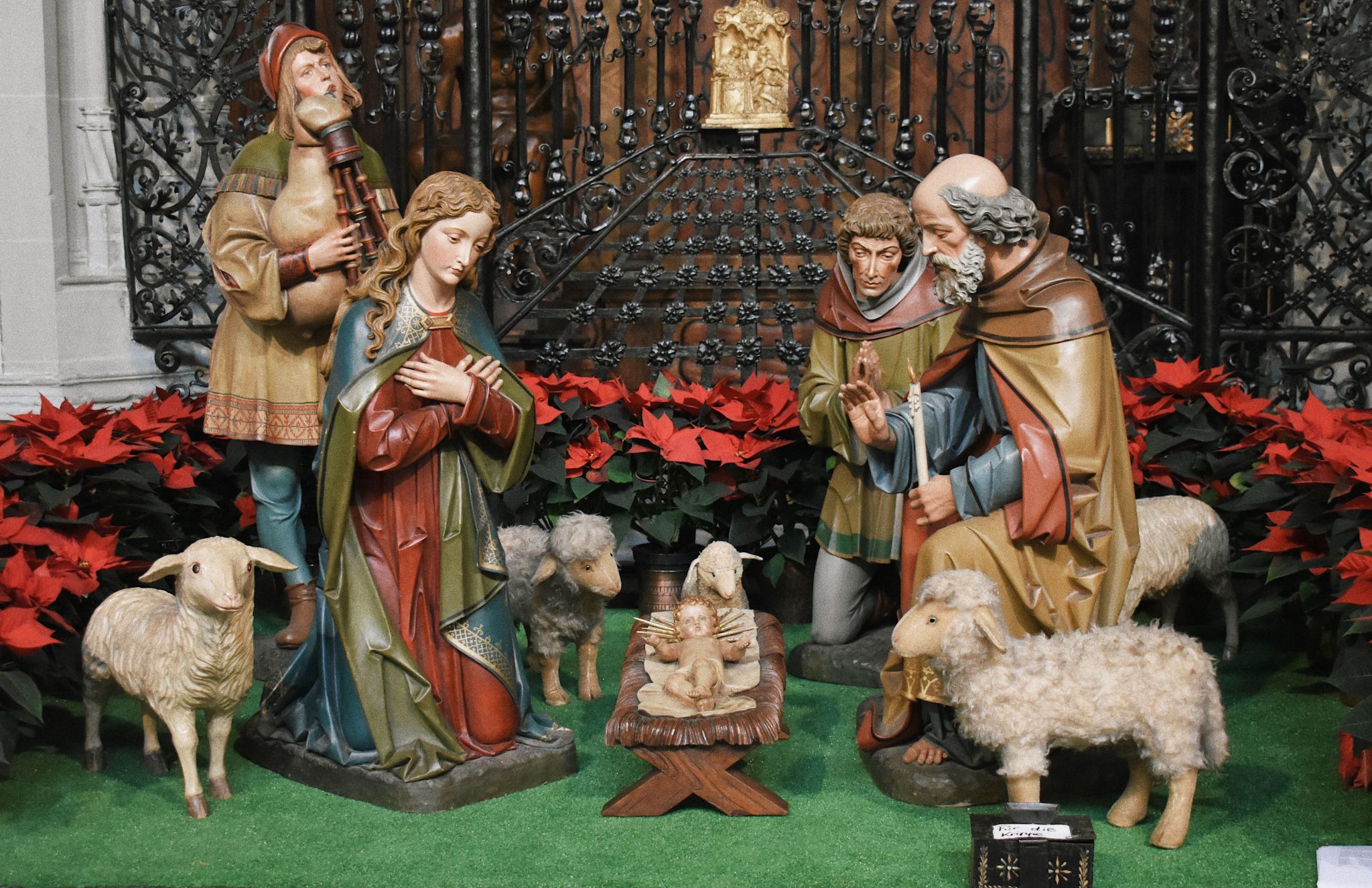 Colorful nativity scene with traditional figurines and red poinsettias.