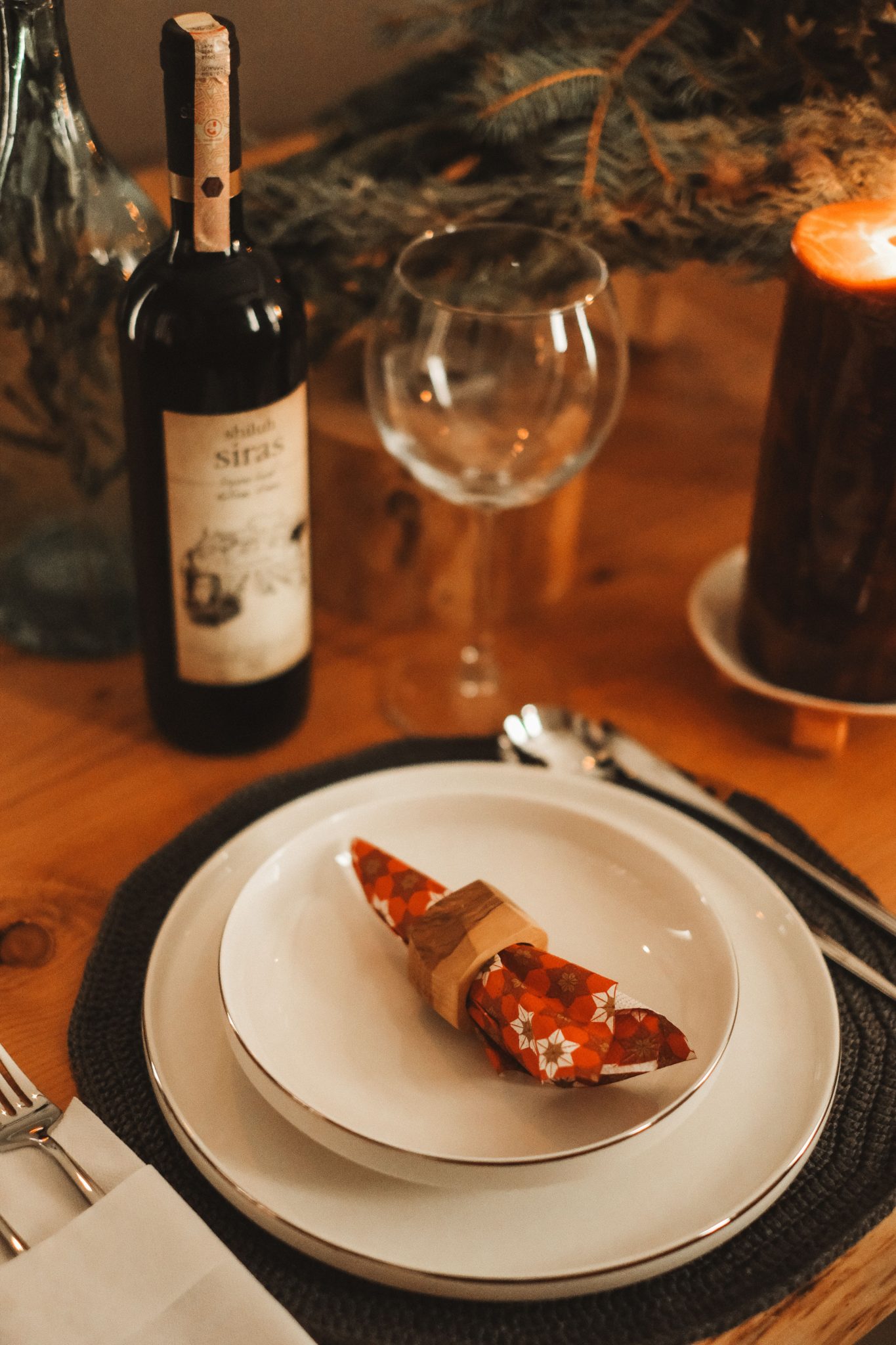 Elegant dinner table setup with wine bottle, glass, and candle light ambiance.