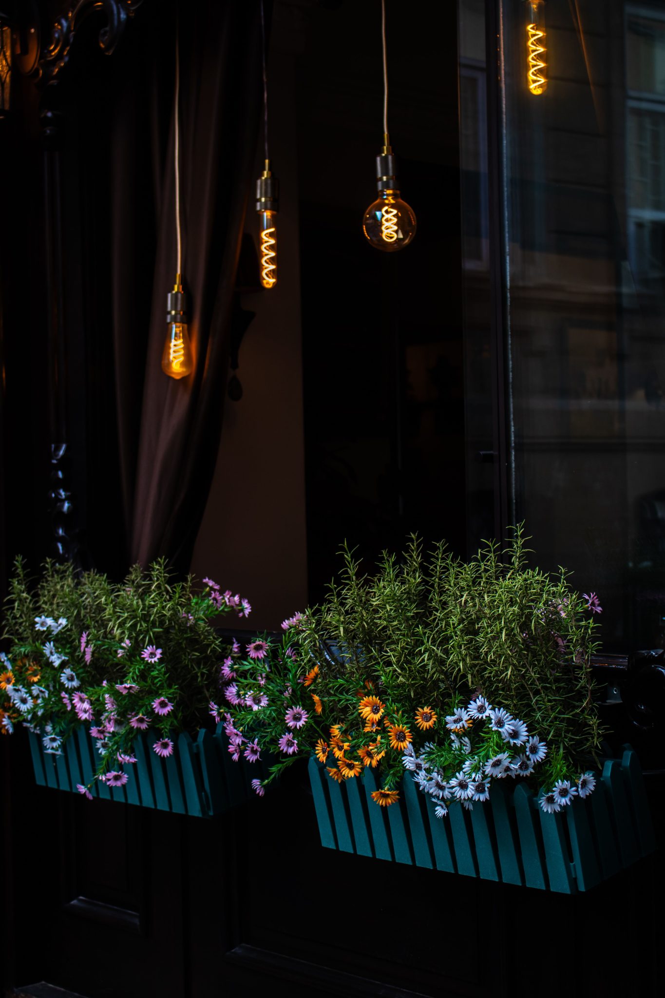 Elegant floral arrangement in planter boxes under warm Edison bulbs at night.