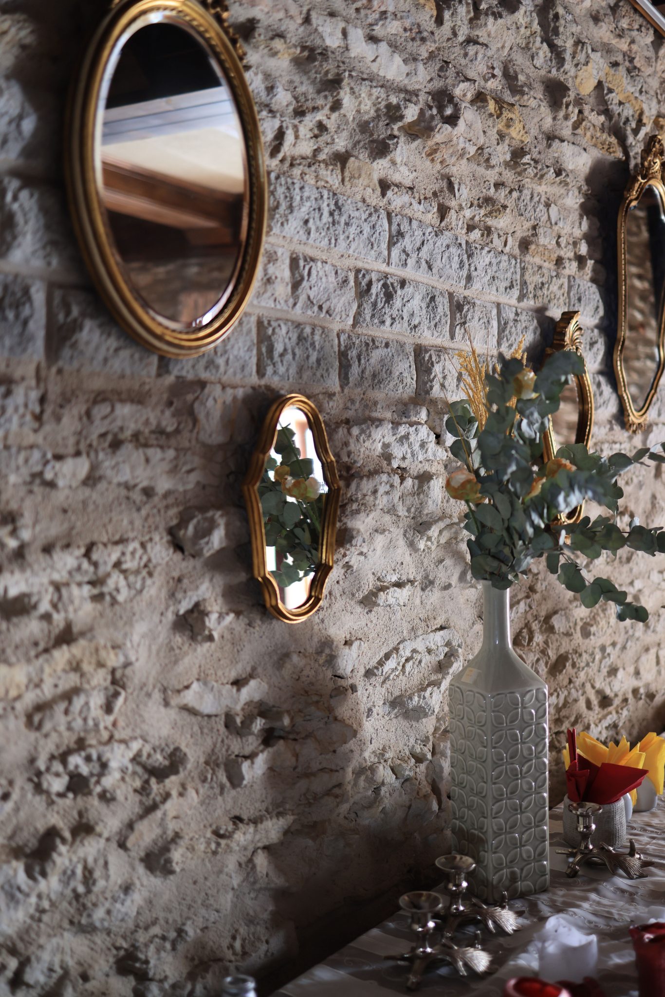 Elegant vintage mirrors and a vase adorn a rustic stone wall, creating a warm decor setting.