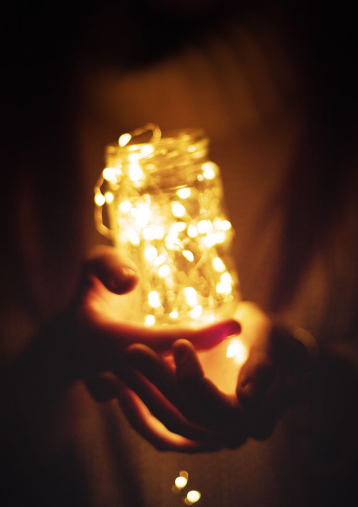 Enchanting hands holding an illuminated glass jar filled with warm string lights, creating a magical glow.