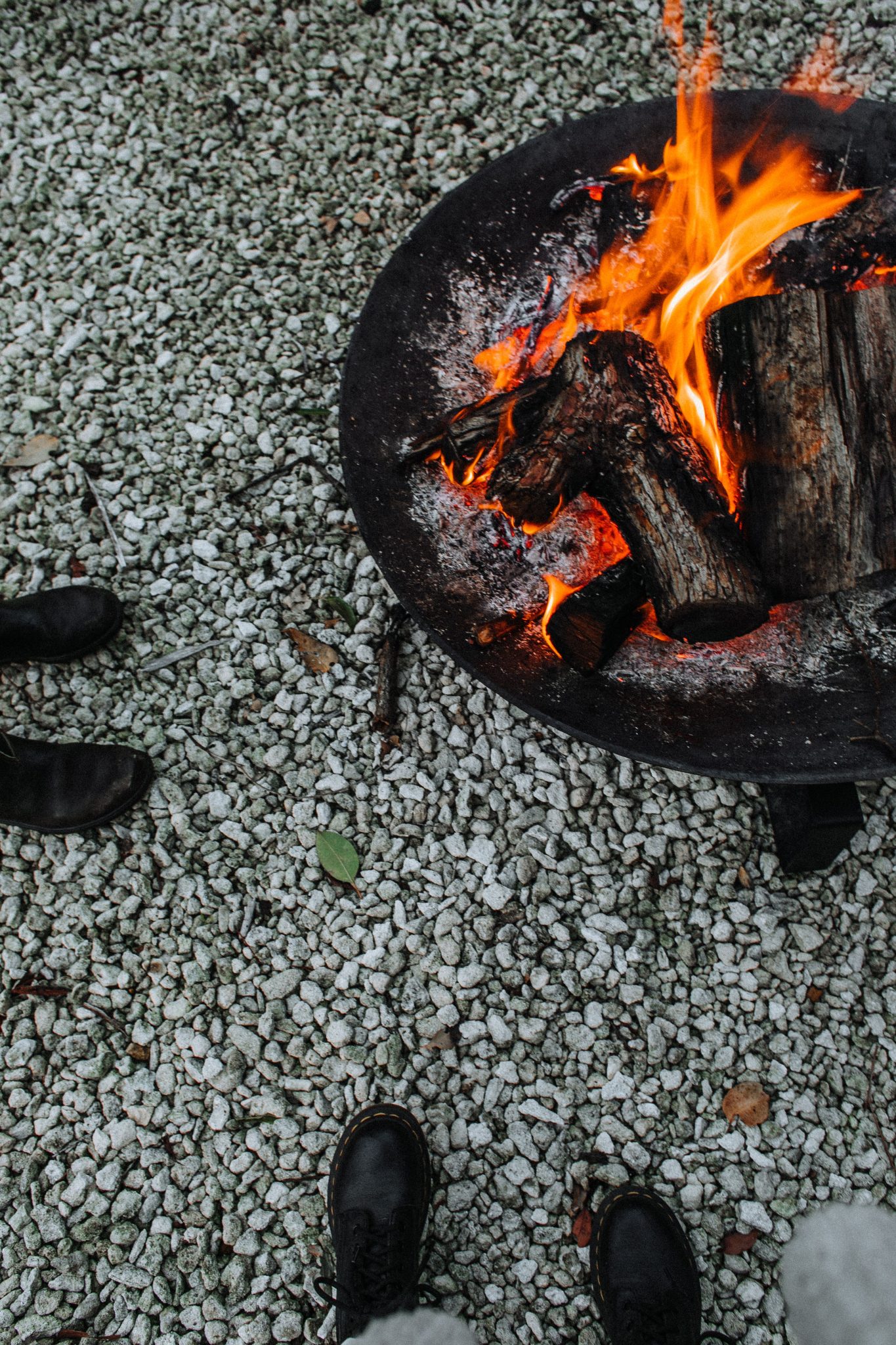 From above of crop anonymous people standing near bonfire with timber and charcoal while warming
