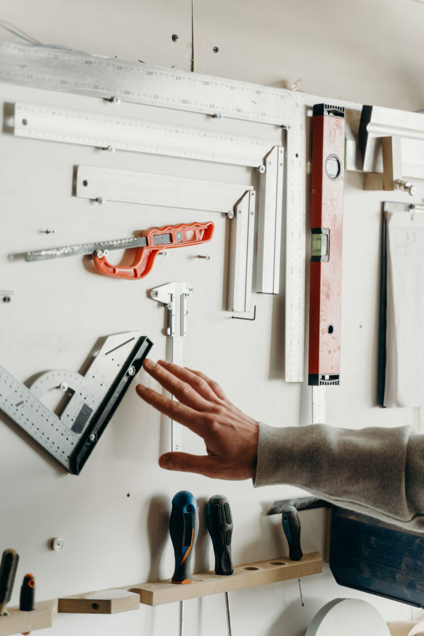 Hand selecting tool from well-organized carpentry wall display. Ideal for woodworking content.