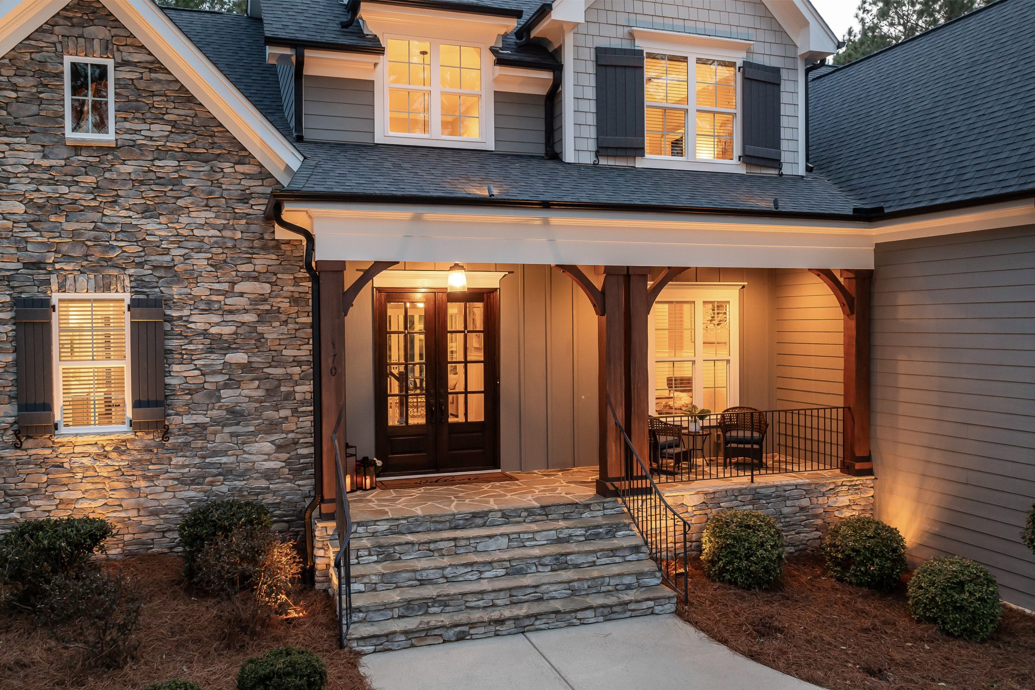 Inviting front porch of a cozy house with stone facade and warm lighting at dusk.