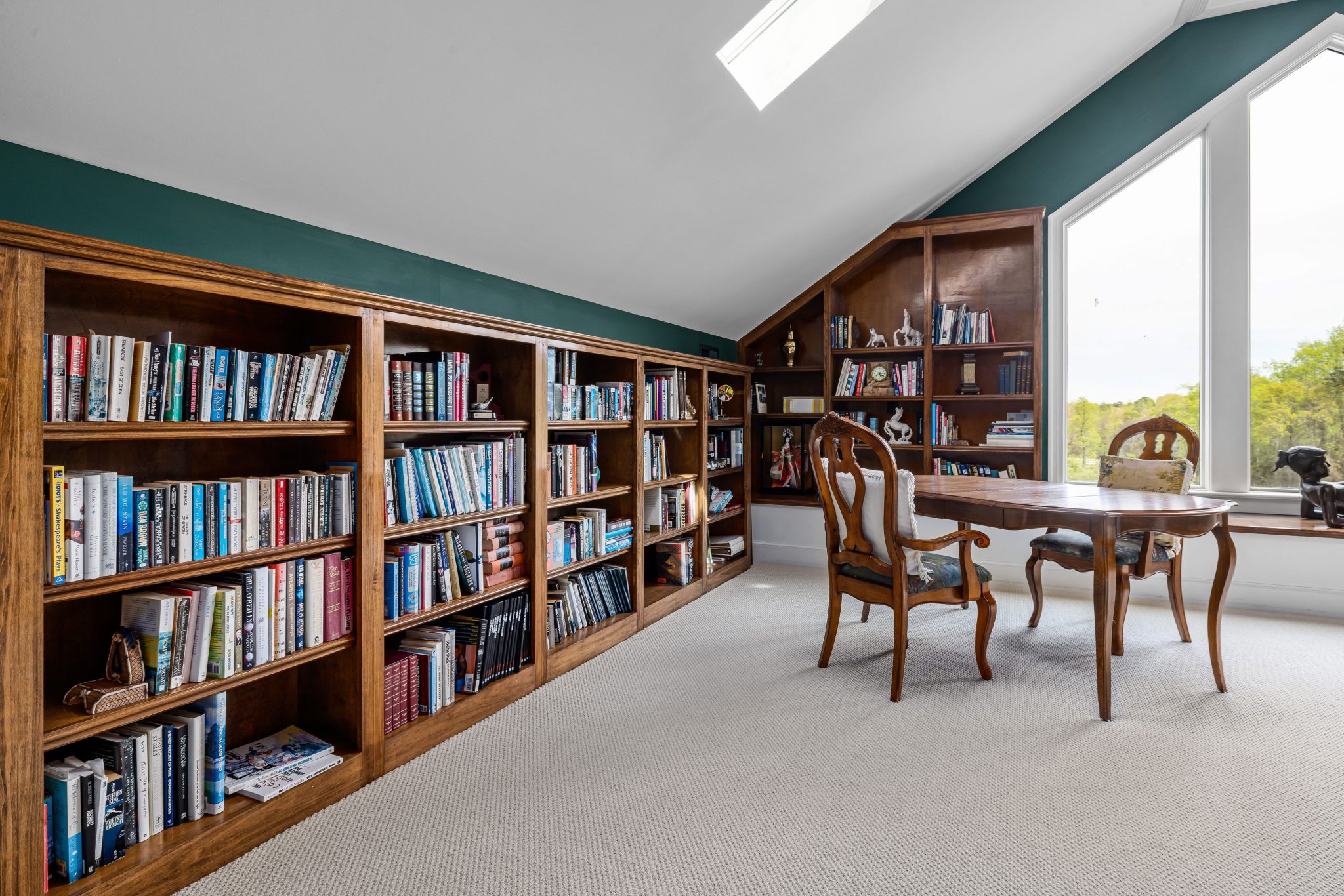 Inviting home library with wooden bookshelves, table, and chairs by a large window.