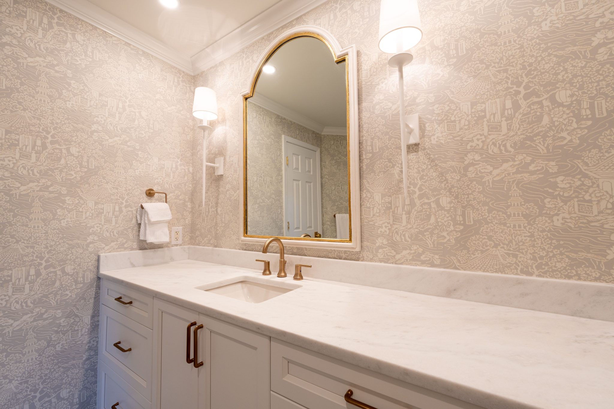 Luxurious bathroom vanity featuring marble countertop, gold fixtures, and decorative wallpaper.
