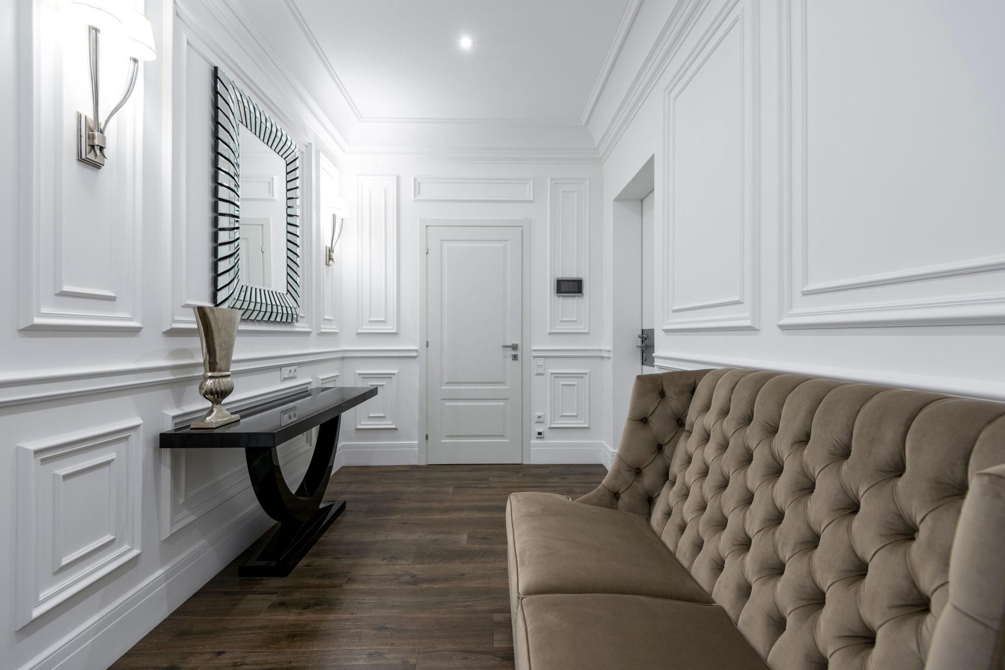 Luxurious white interior featuring a modern tufted sofa and classic wall paneling.