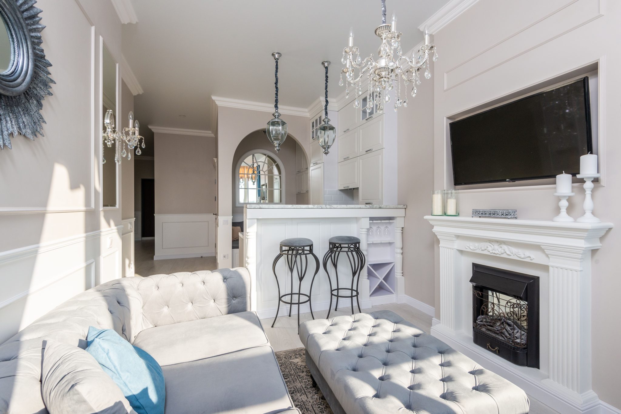 Modern room interior with sofa and textile bench against fireplace under candles and television in sunlight