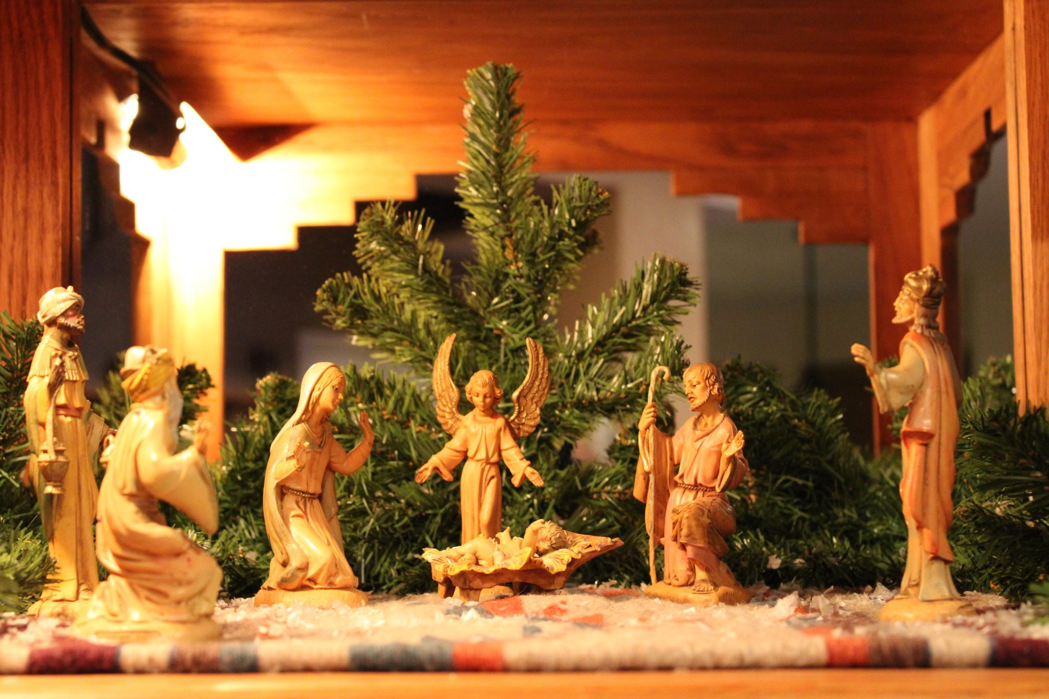 Nativity scene with figurines and Christmas tree in warm indoor setting.