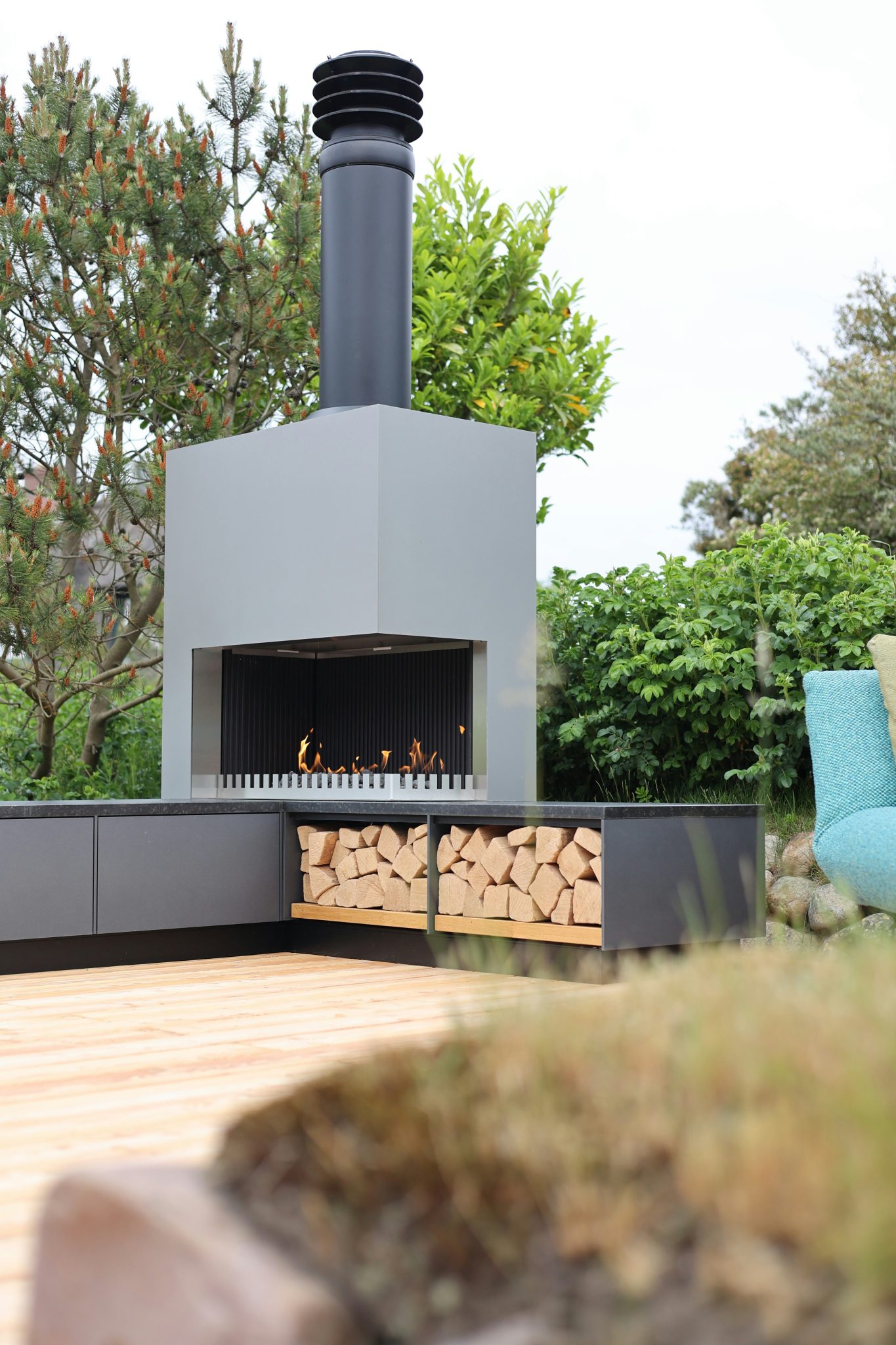 Outdoor fireplace with burning logs and firewood on a deck