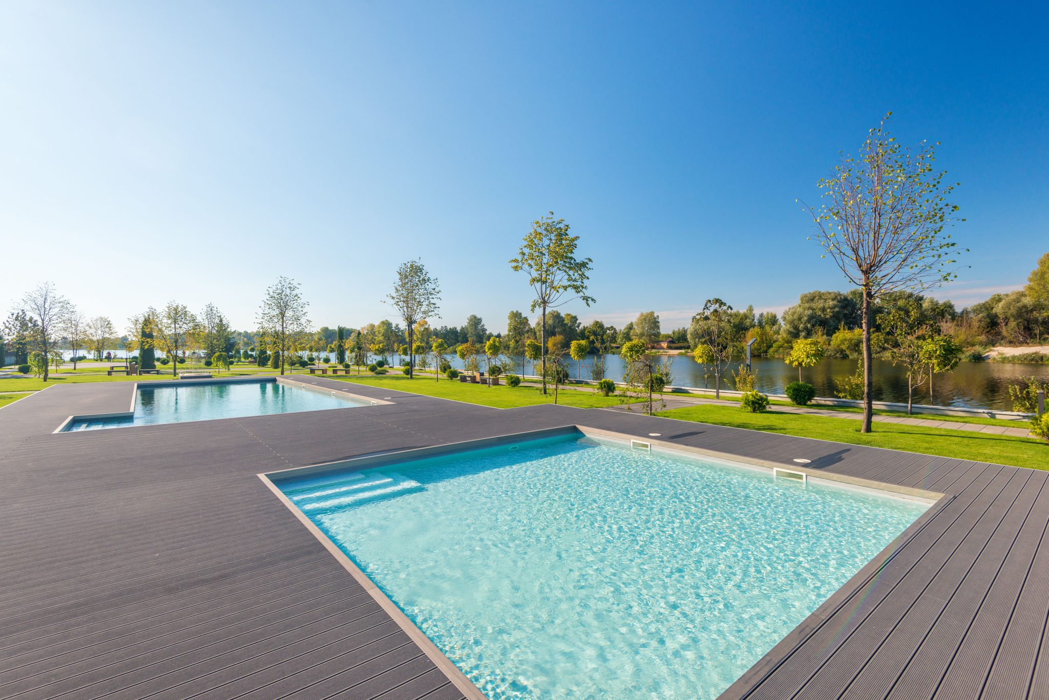 Relaxing poolside scene with a clear sky, lush trees, and a tranquil river backdrop.