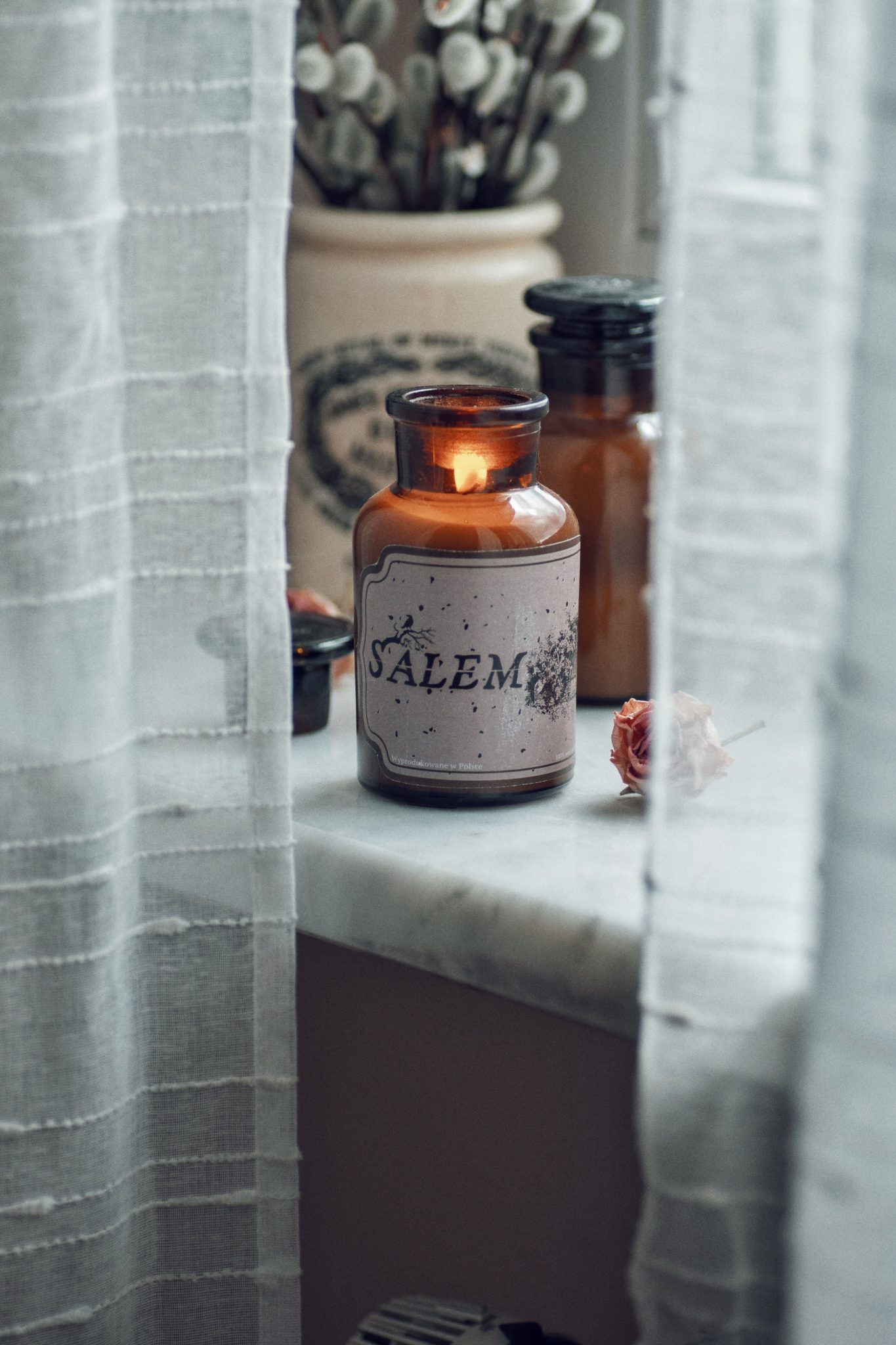 Rustic amber bottle labeled 'Salem' on a marble windowsill with dried flowers.