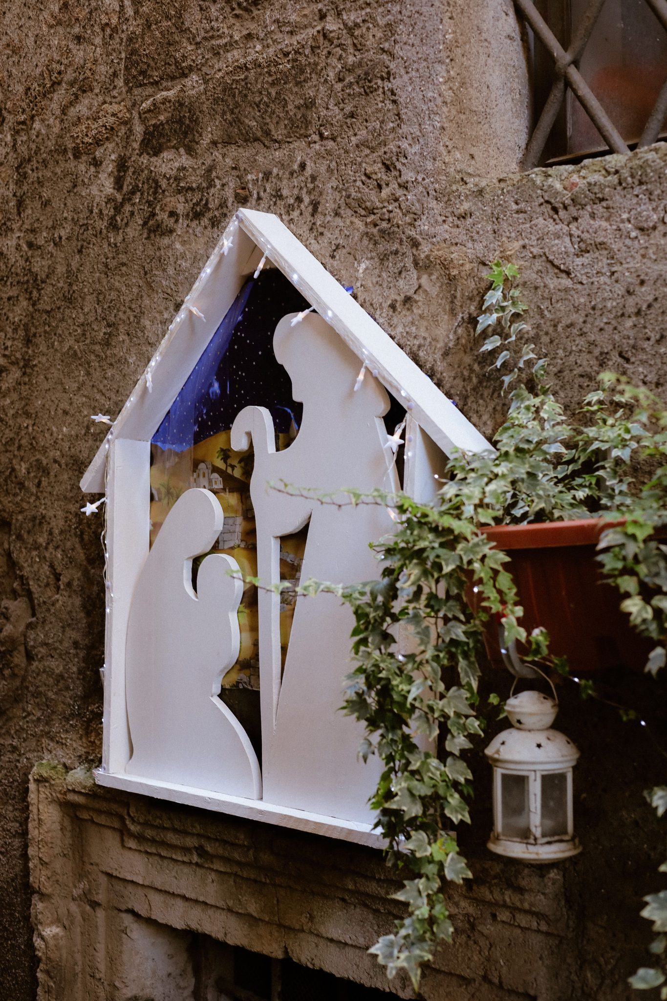 Rustic nativity scene with lantern and greenery in outdoor setting.