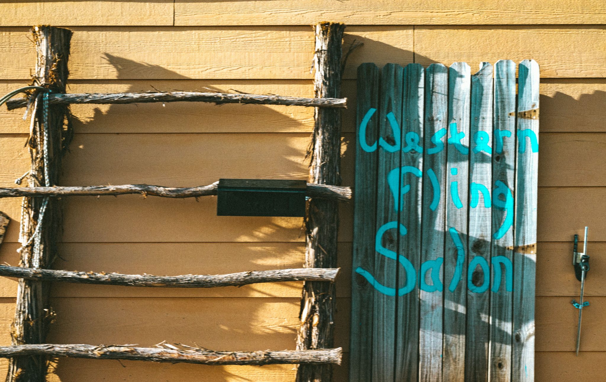 Rustic wooden sign for Western Flng Saloon on a sunny day outdoors.