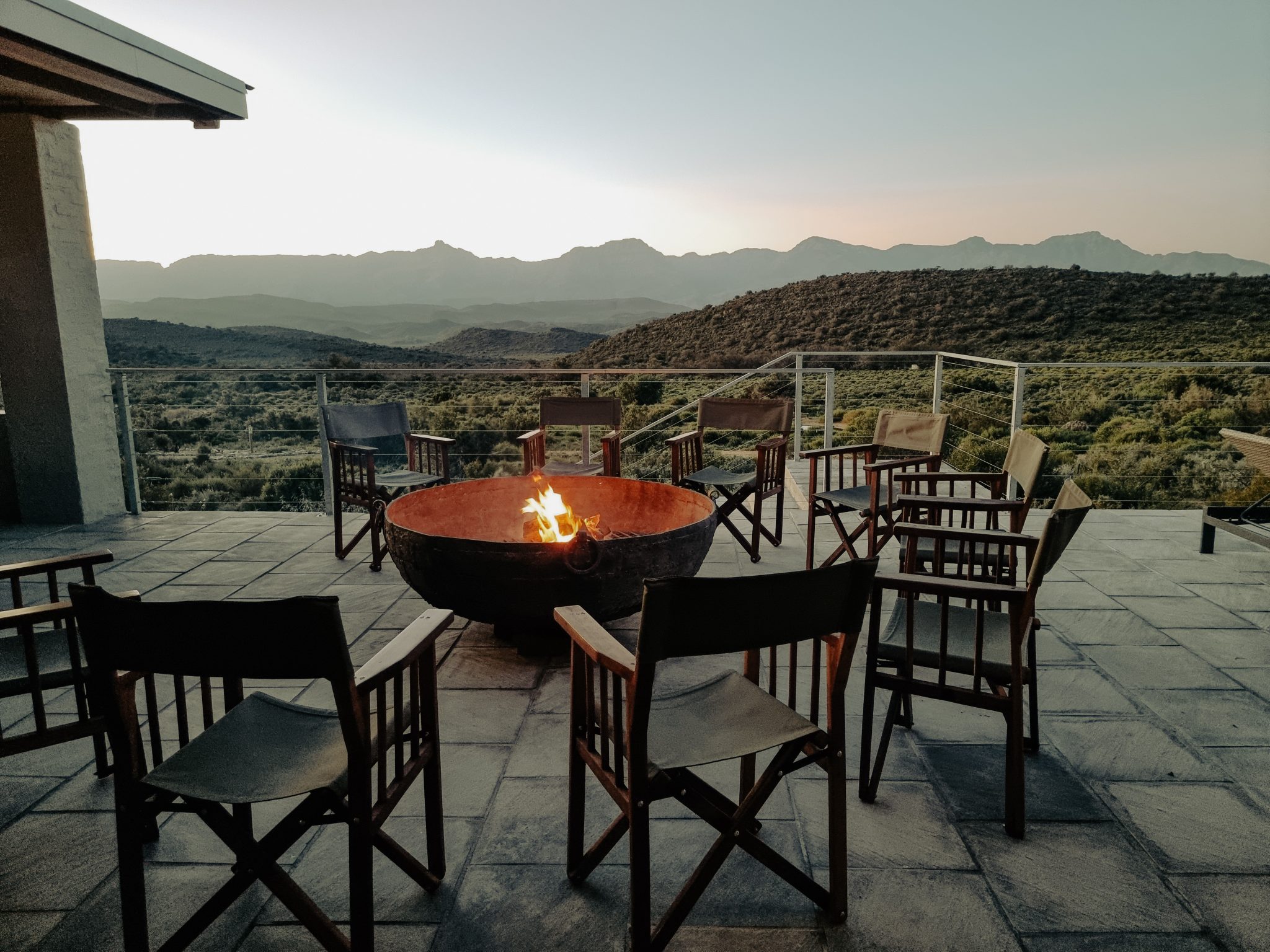 Scenic mountain view from a cozy balcony with a blazing fire pit surrounded by chairs.