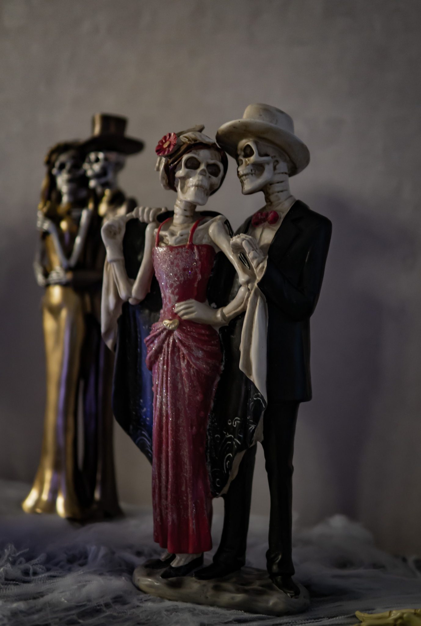 Skeleton figurines dressed in formal attire, ideal for Halloween decor, set against a gray background.