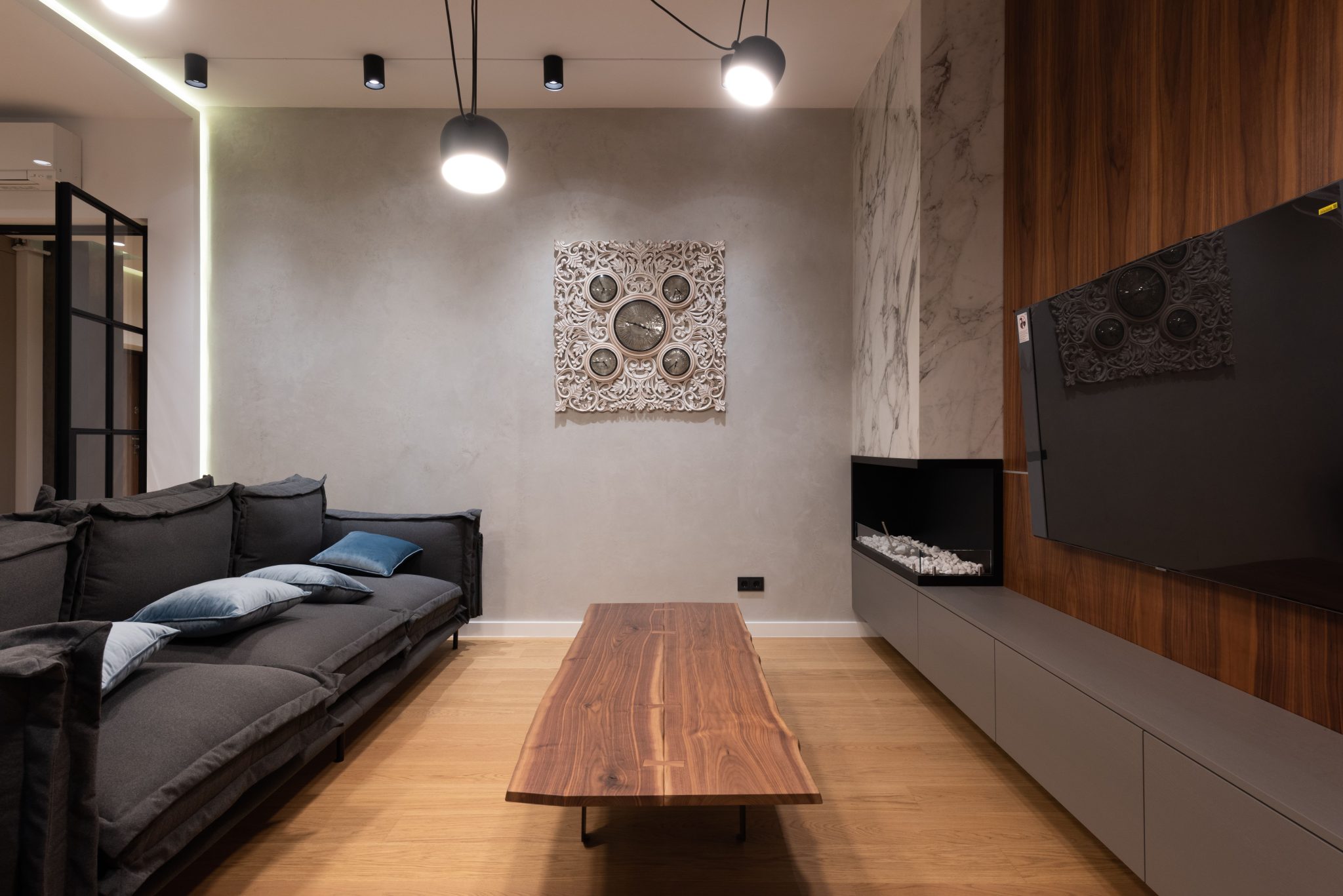 Soft couch with cushions placed against wooden coffee table and modern TV set hanging on wooden wall near fireplace in spacious living room