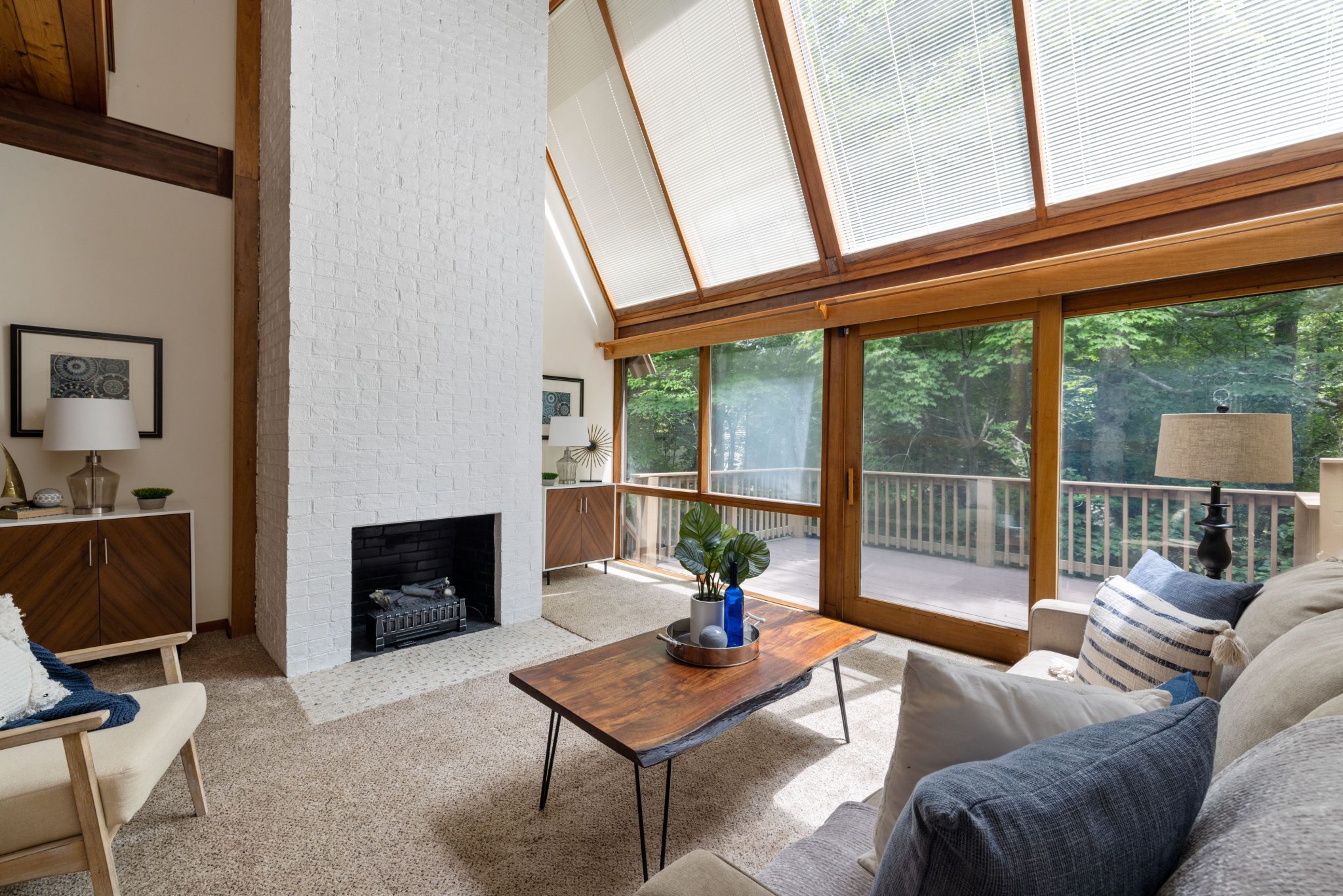 Spacious living room features a white brick fireplace and floor-to-ceiling windows overlooking greenery.