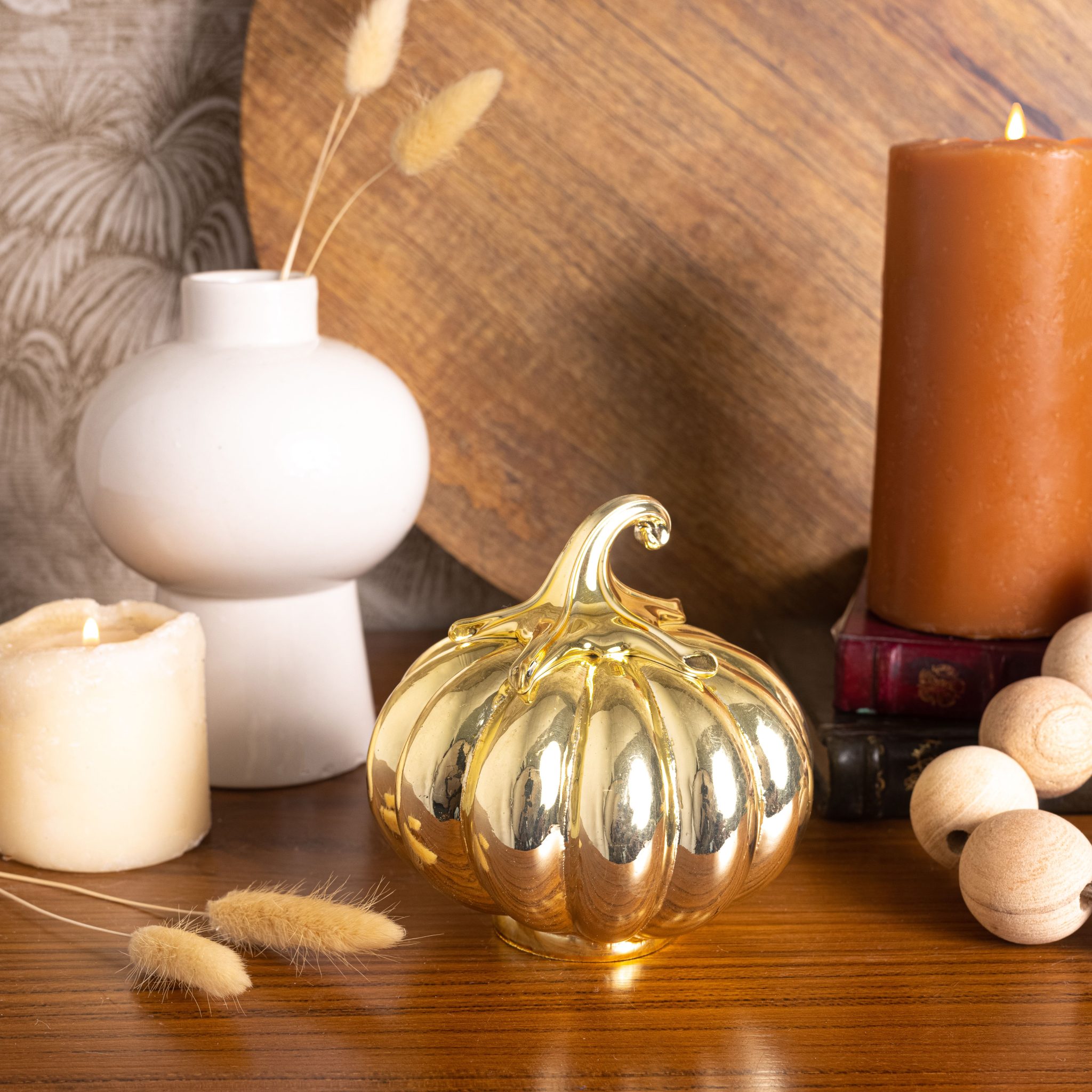 Stylish fall tabletop decoration featuring a golden pumpkin, candles, and modern vase in cozy indoor setting.