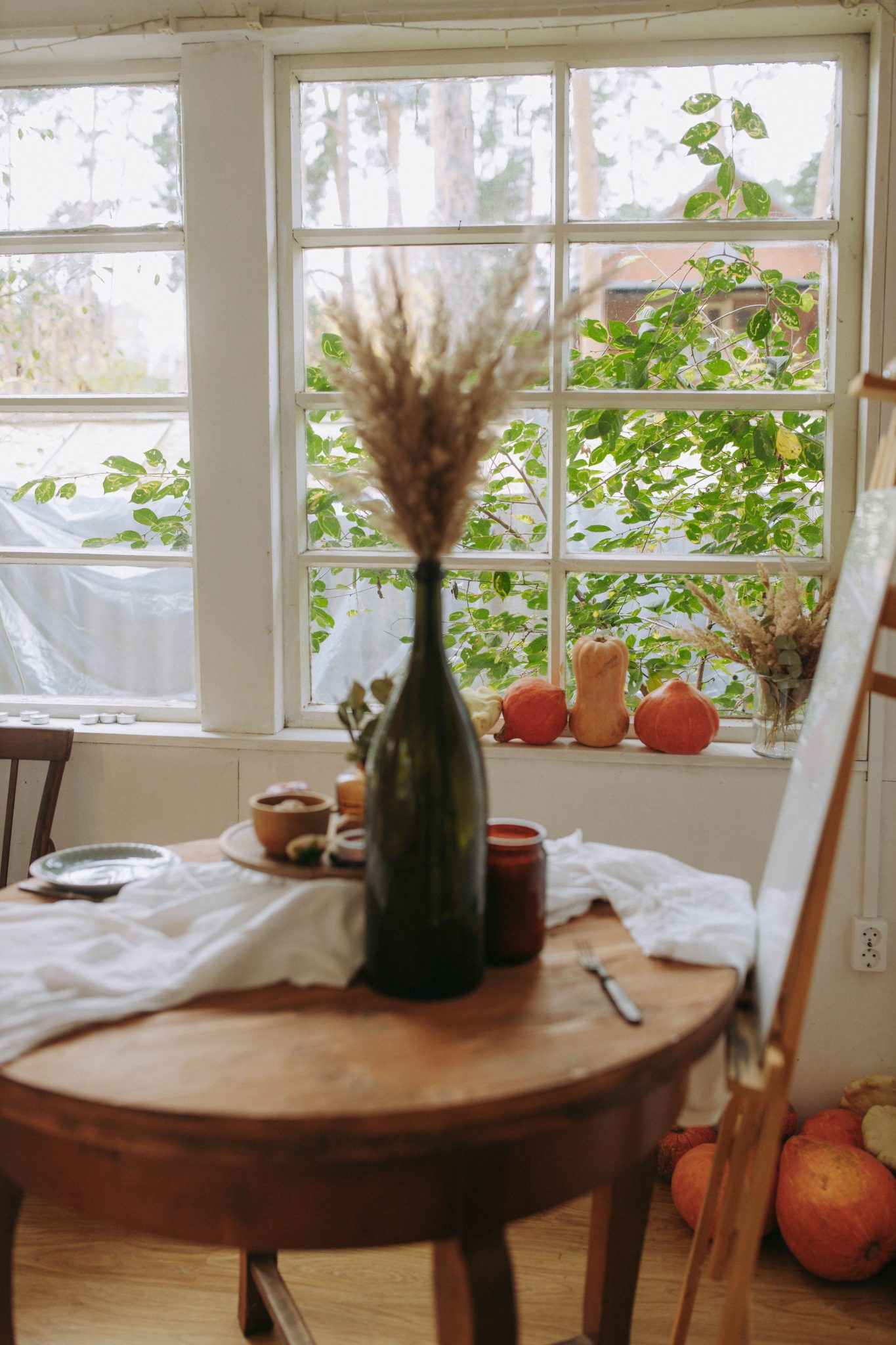Sunlit room with autumn decor featuring pumpkins and dried flowers on a wooden table.