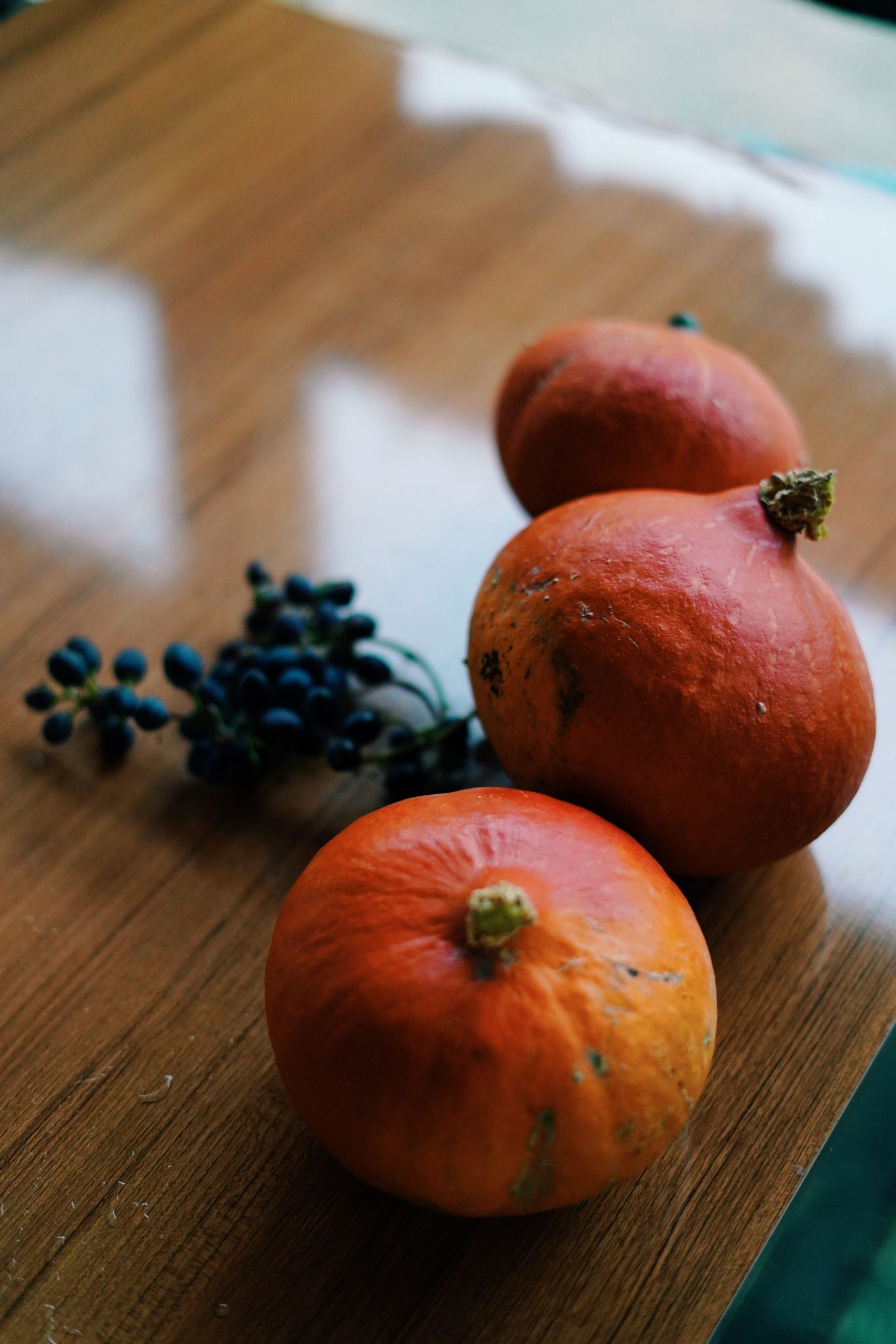 Three decorative pumpkins and berries on a wooden surface, evoking a cozy fall vibe.