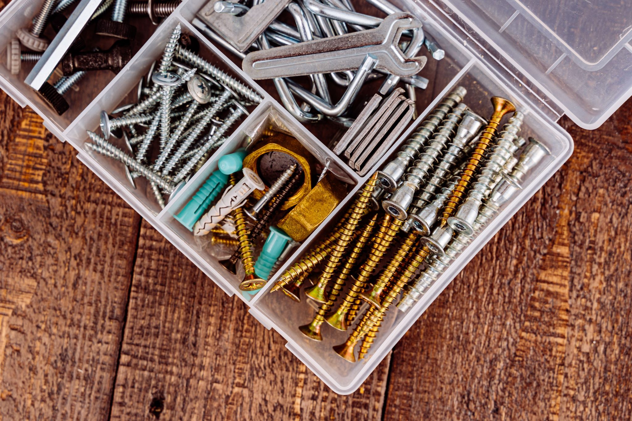 Top view of assorted screws and tools in a plastic organizer on wooden surface.