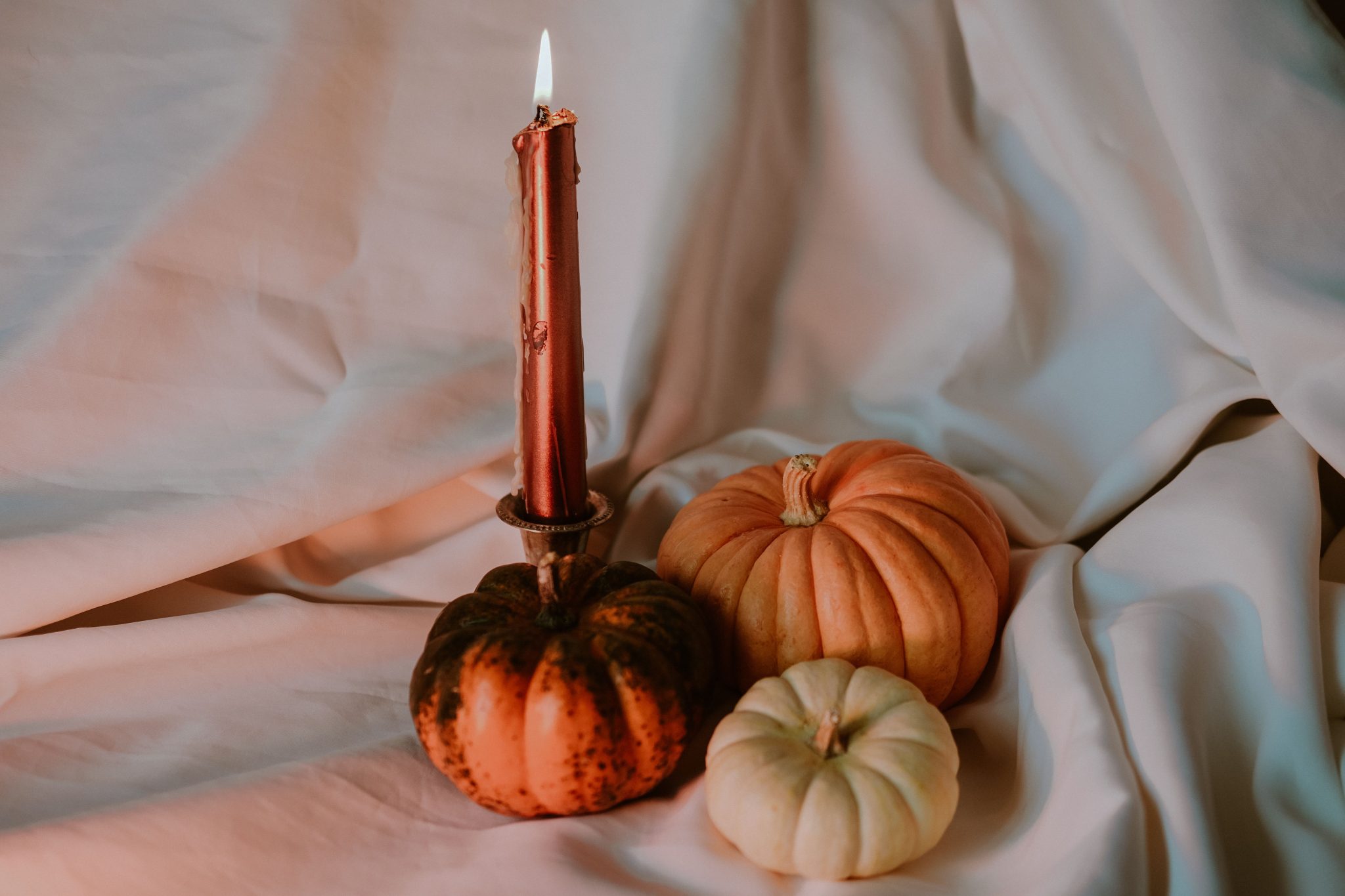 Warm and cozy still life of pumpkins and a lit candle on a soft fabric background.