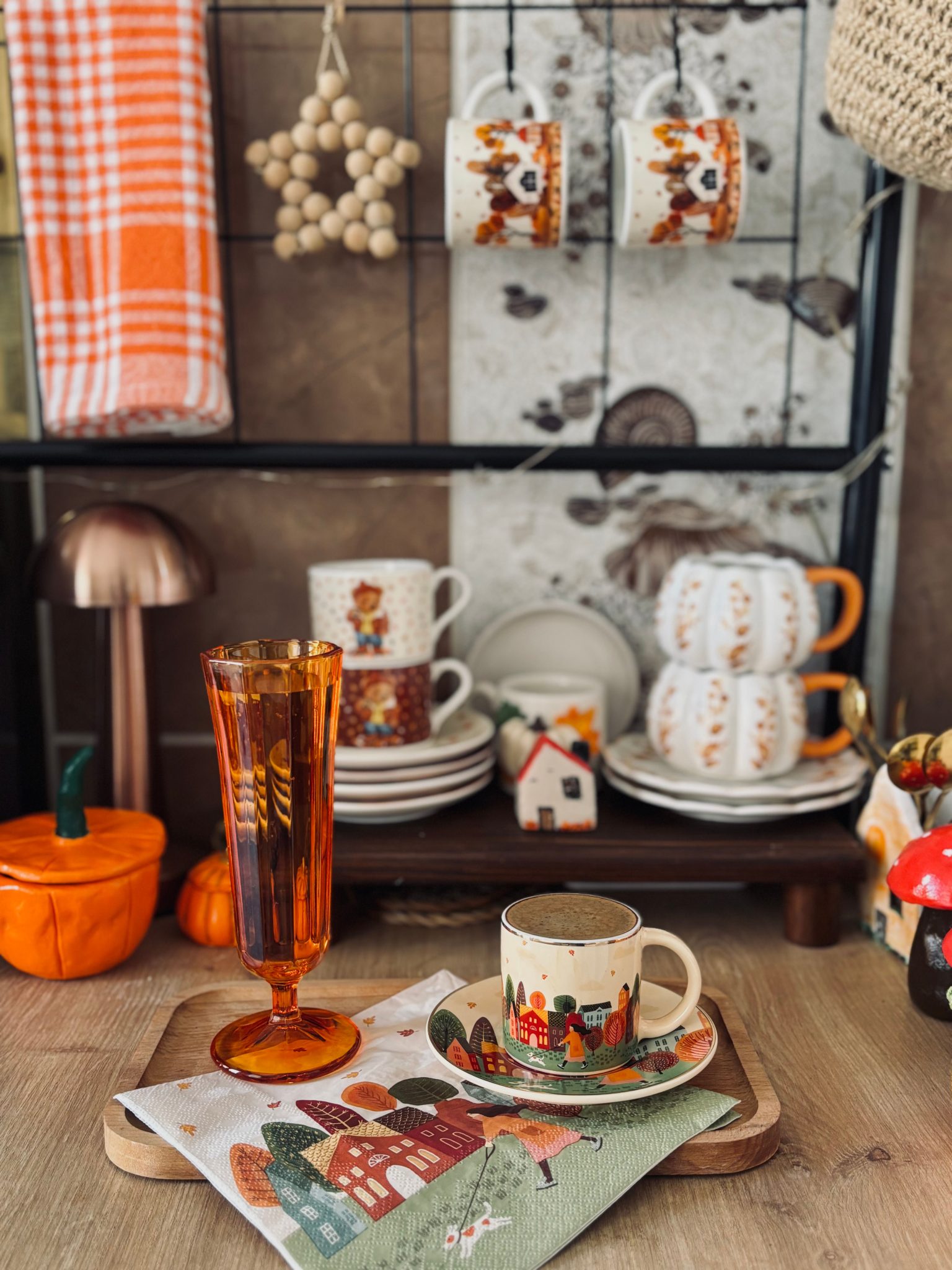 Warm autumn-inspired kitchen decor with cups and pumpkins.
