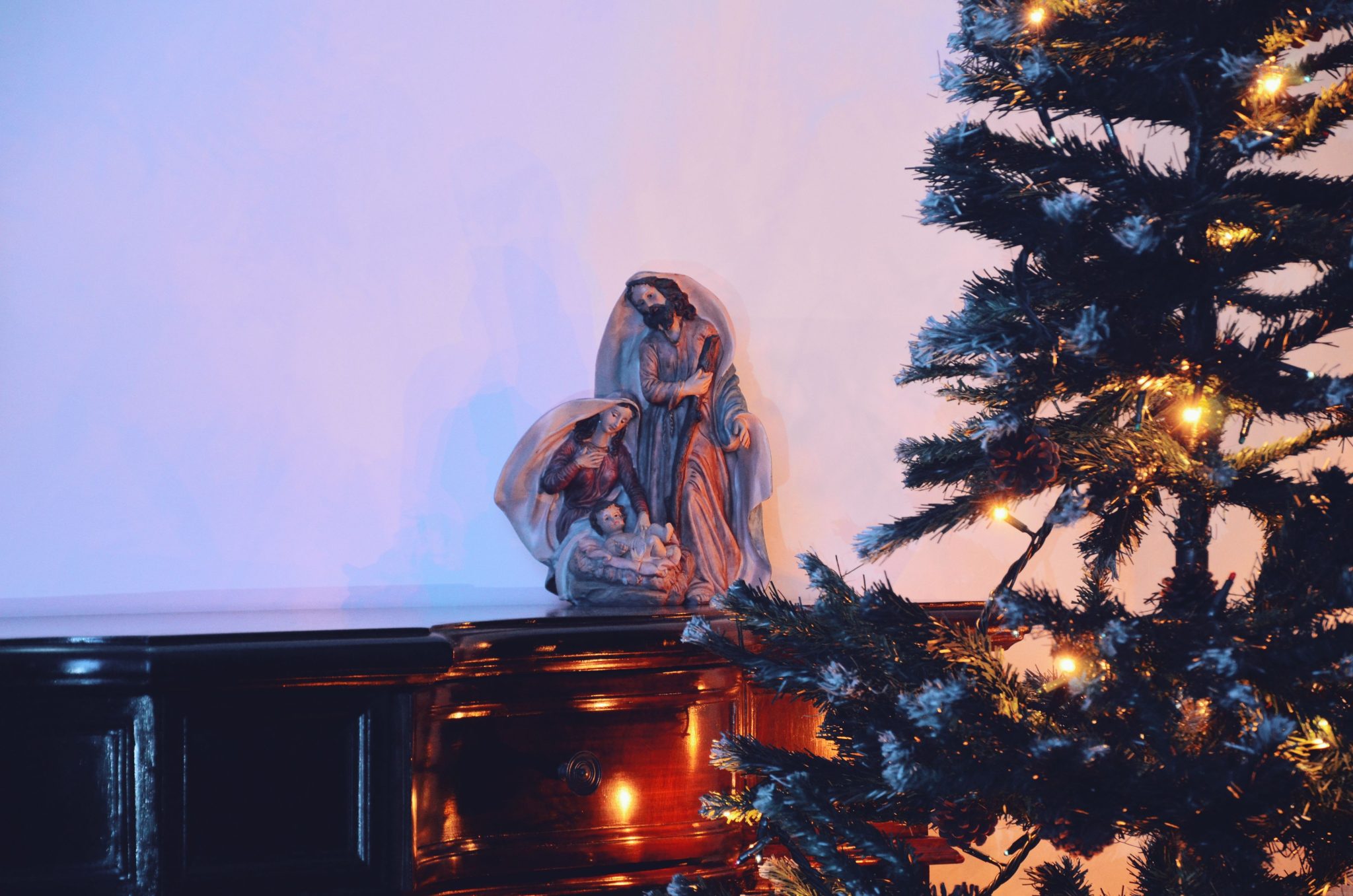 Warm Christmas setup featuring a nativity scene and a decorated tree with lights on a wooden table.
