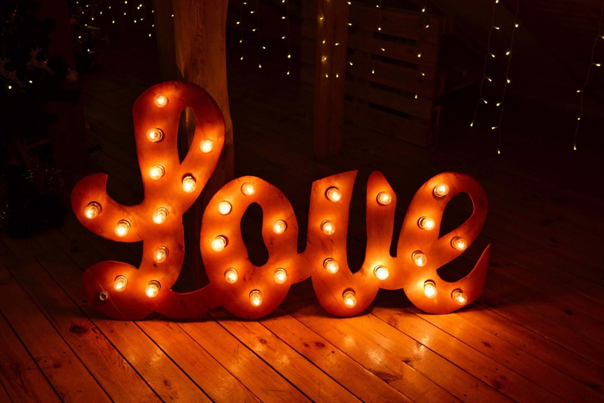 Warm, glowing 'Love' sign with bulb lights on wooden floorboards, perfect for romantic settings.