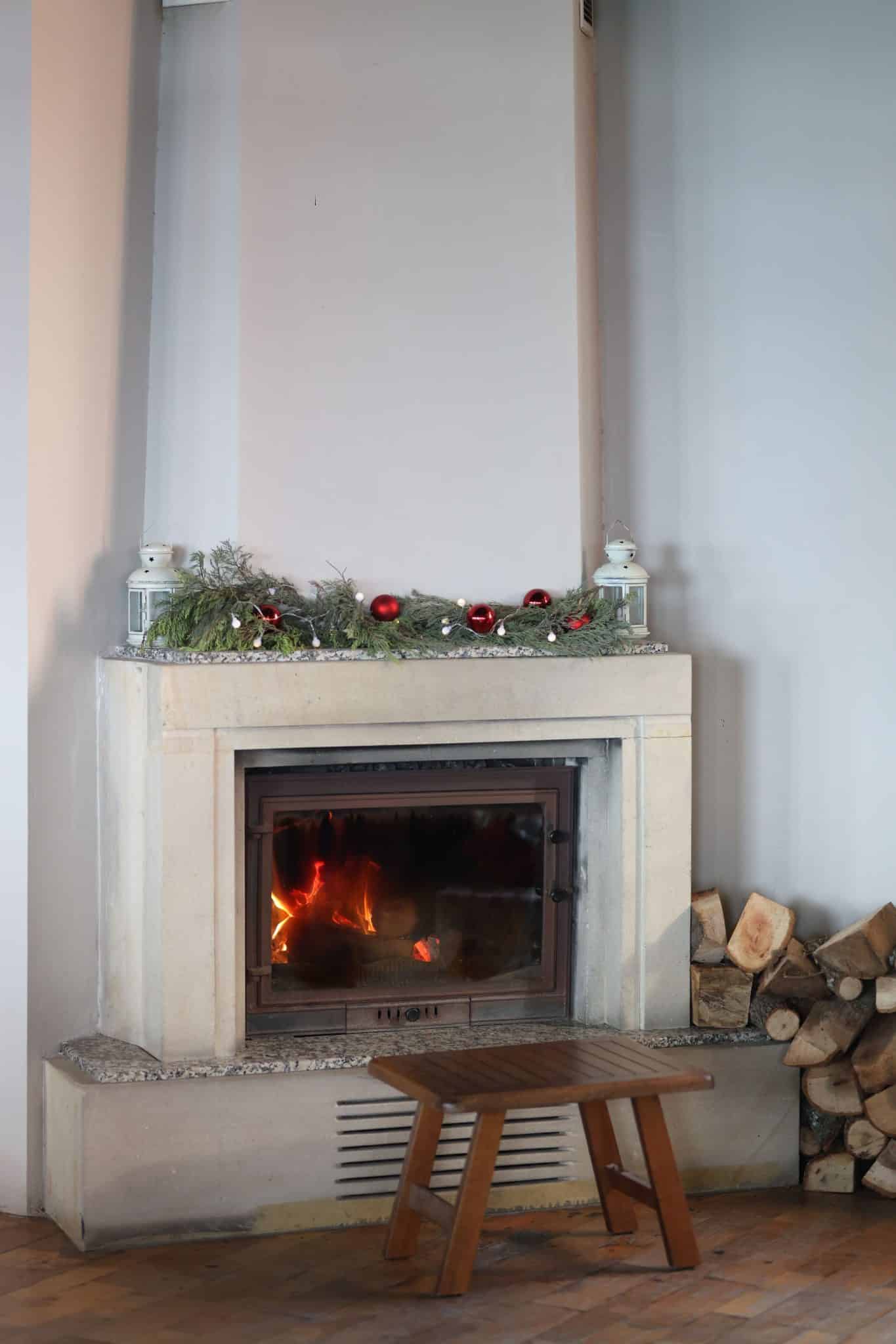 Warm indoor scene with a lit fireplace decorated with Christmas ornaments and greenery.