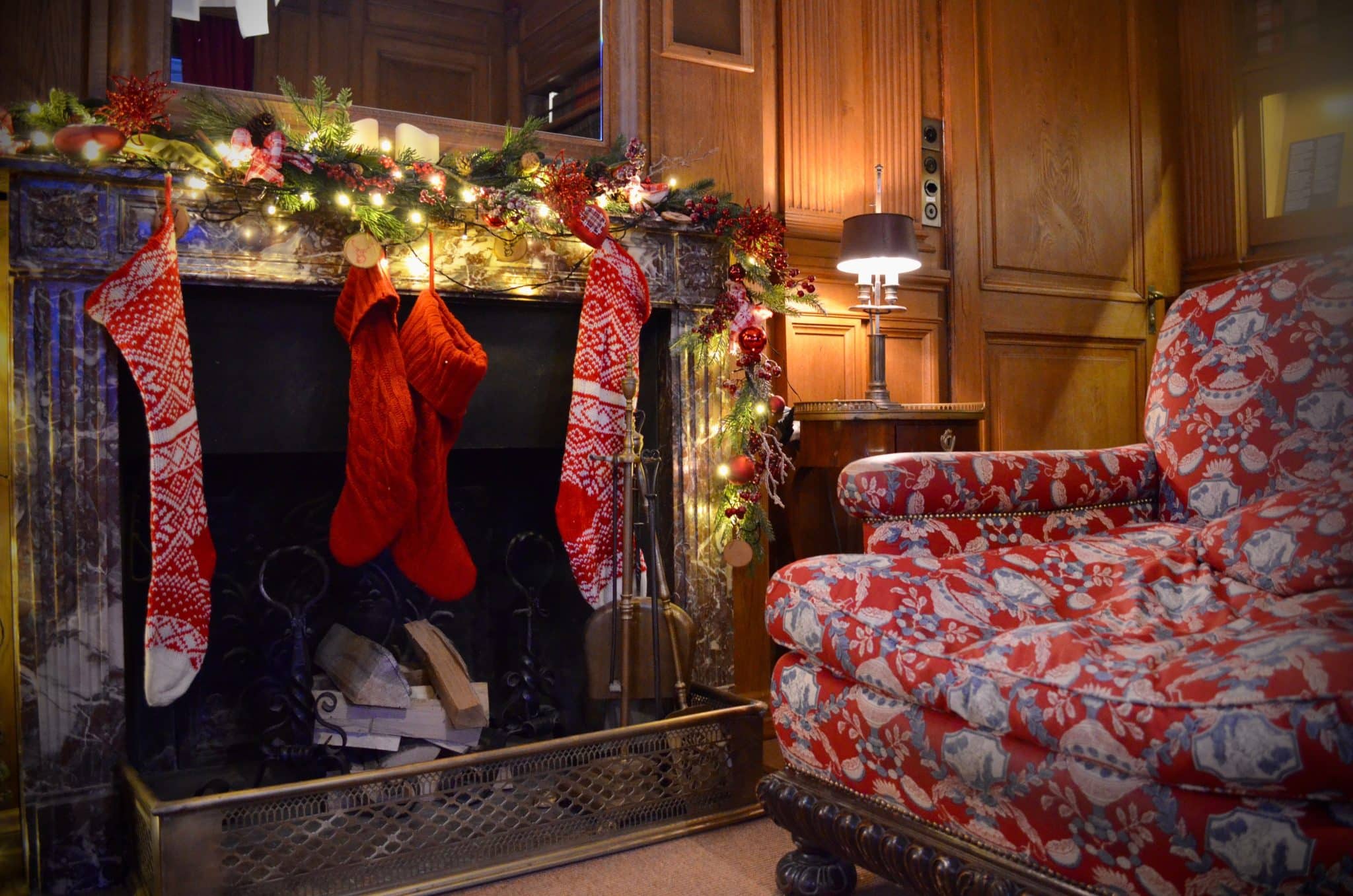 Warm living room with Christmas stockings by the fireplace, festive garland, and cozy chair.